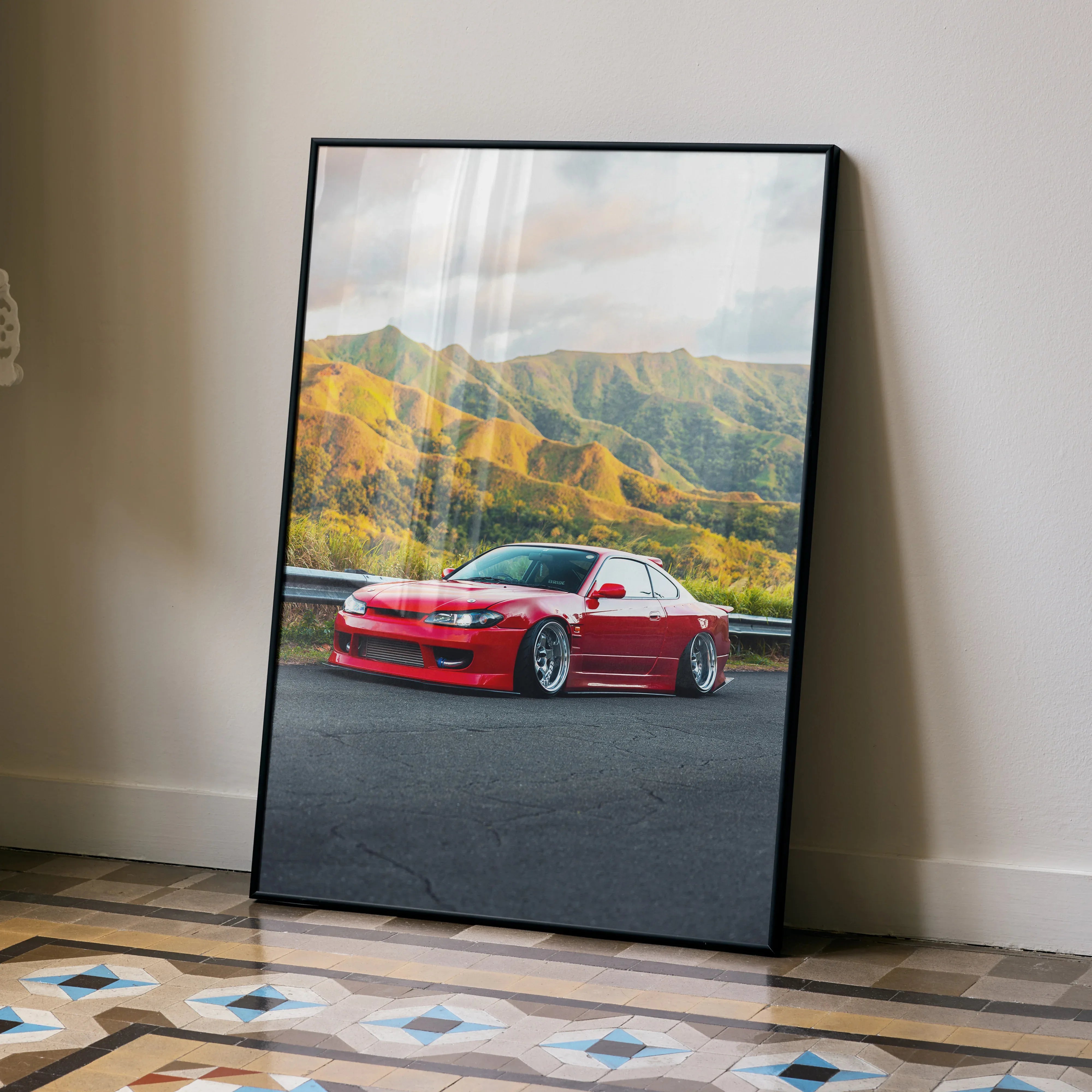 Nissan Silvia S15 poster with red car and mountain landscape wall art in black frame leaning on floor.