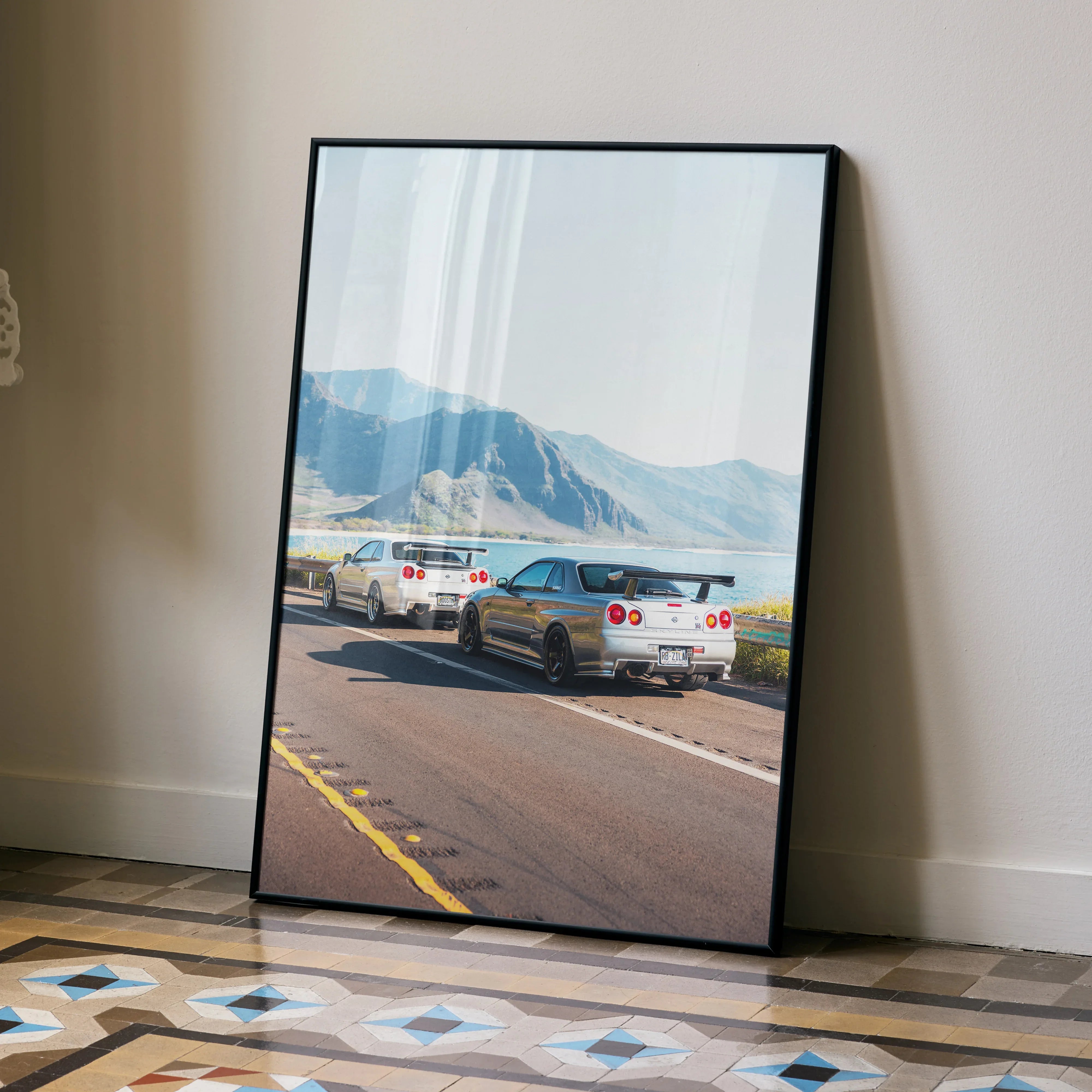 Nissan GT-R R34 Skyline on mountain road poster leaning against beige wall, automotive wall art.