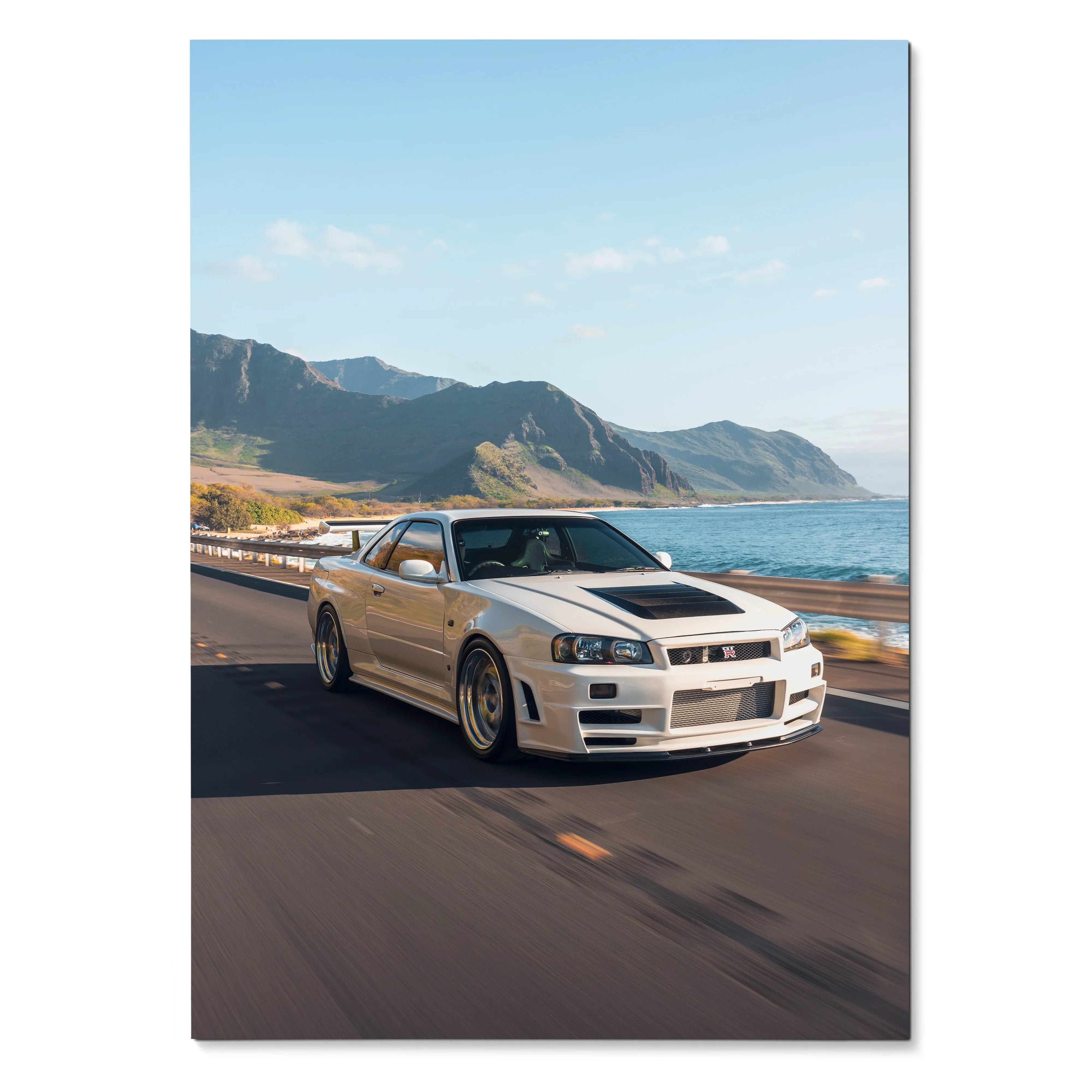 Nissan R34 GT-R driving on coastal road poster wall art with mountains and ocean background.