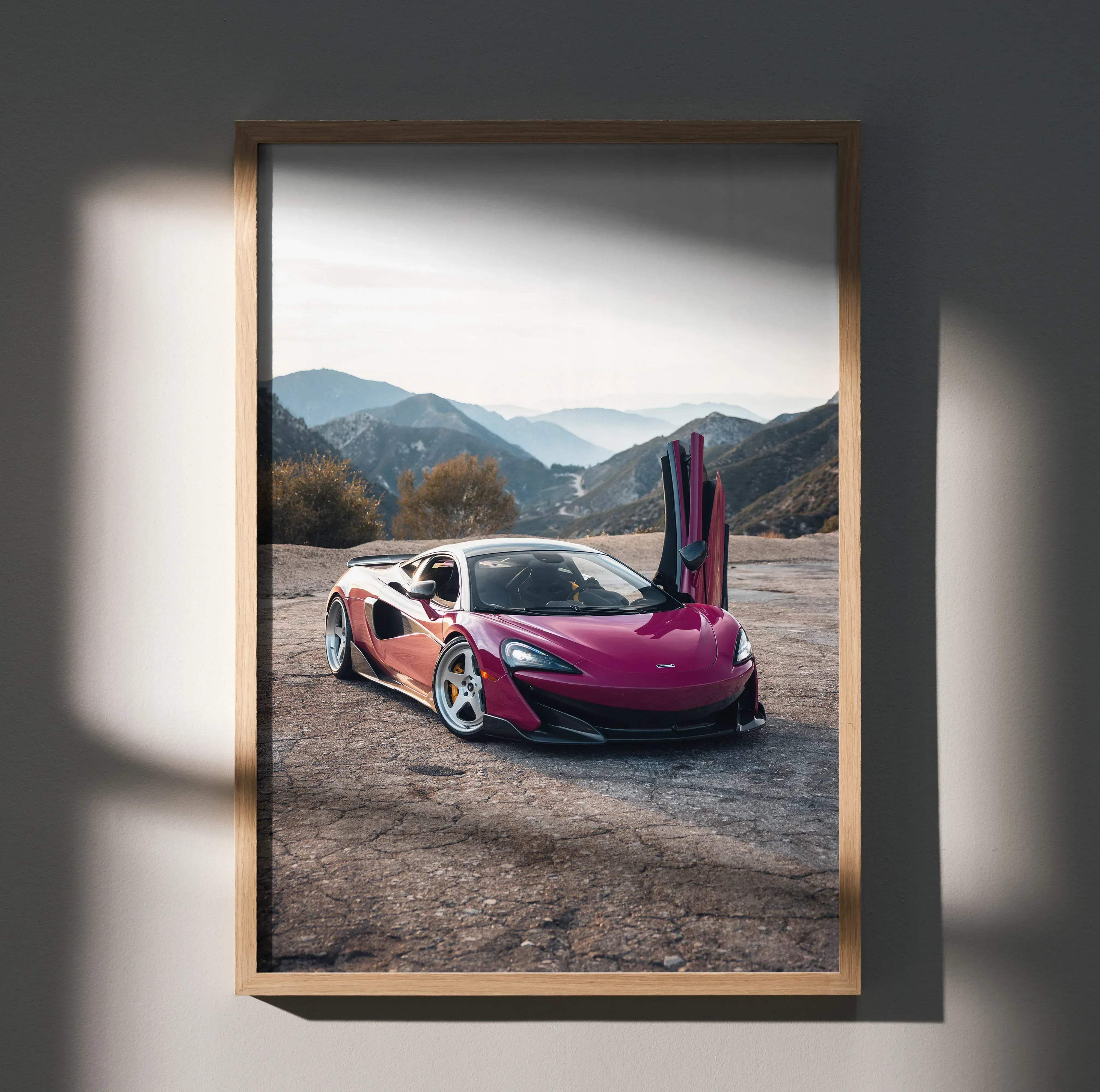 A vibrant pink McLaren 570s sports car with butterfly doors open in a rugged mountainous landscape poster