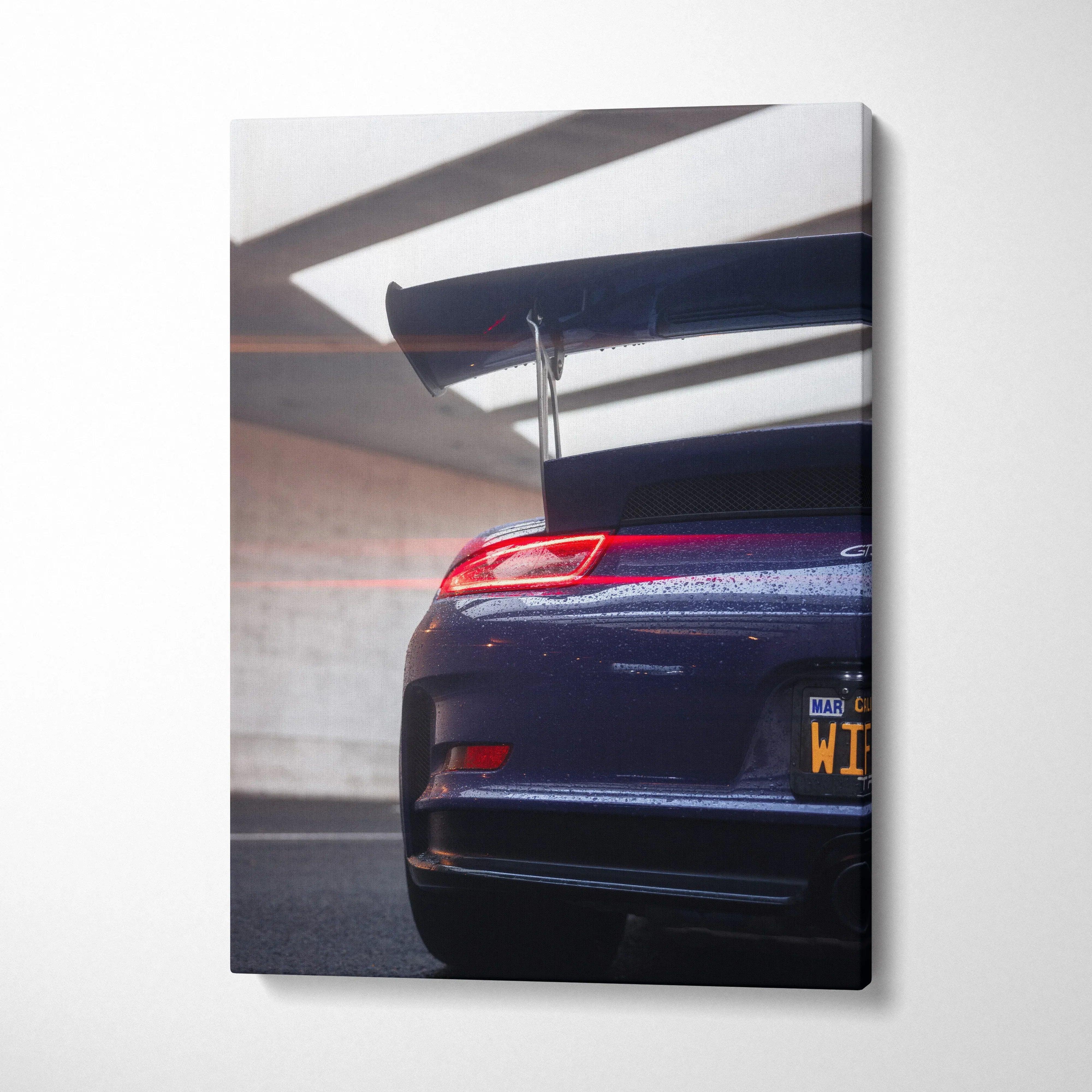 Vertical canvas wall art featuring the rear end and spoiler of a dark blue Porsche 911 GT3 RS in a garage.