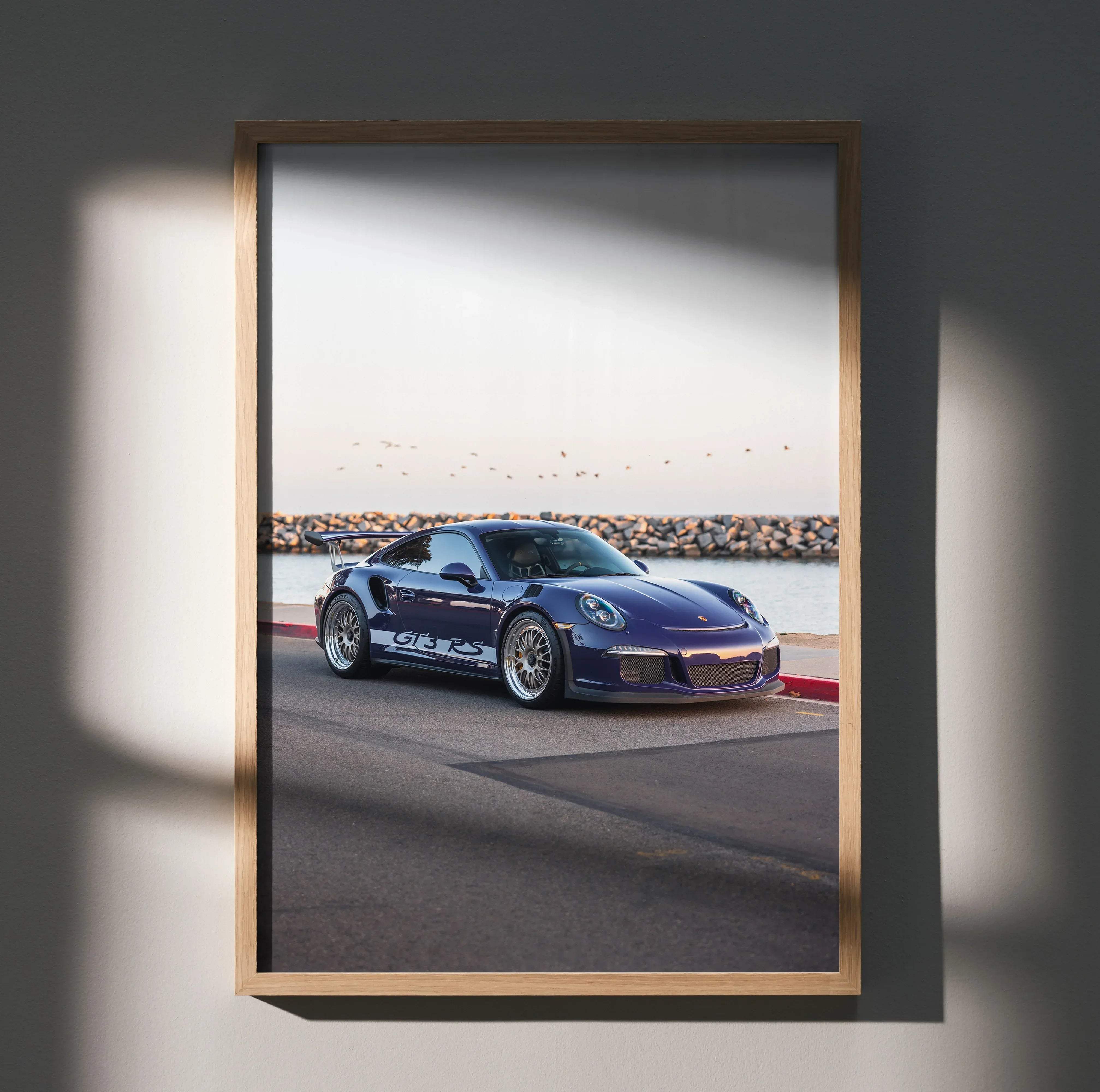 A framed photograph of a deep purple Porsche 911 GT3 RS sports car with silver racing stripes in a light wood frame