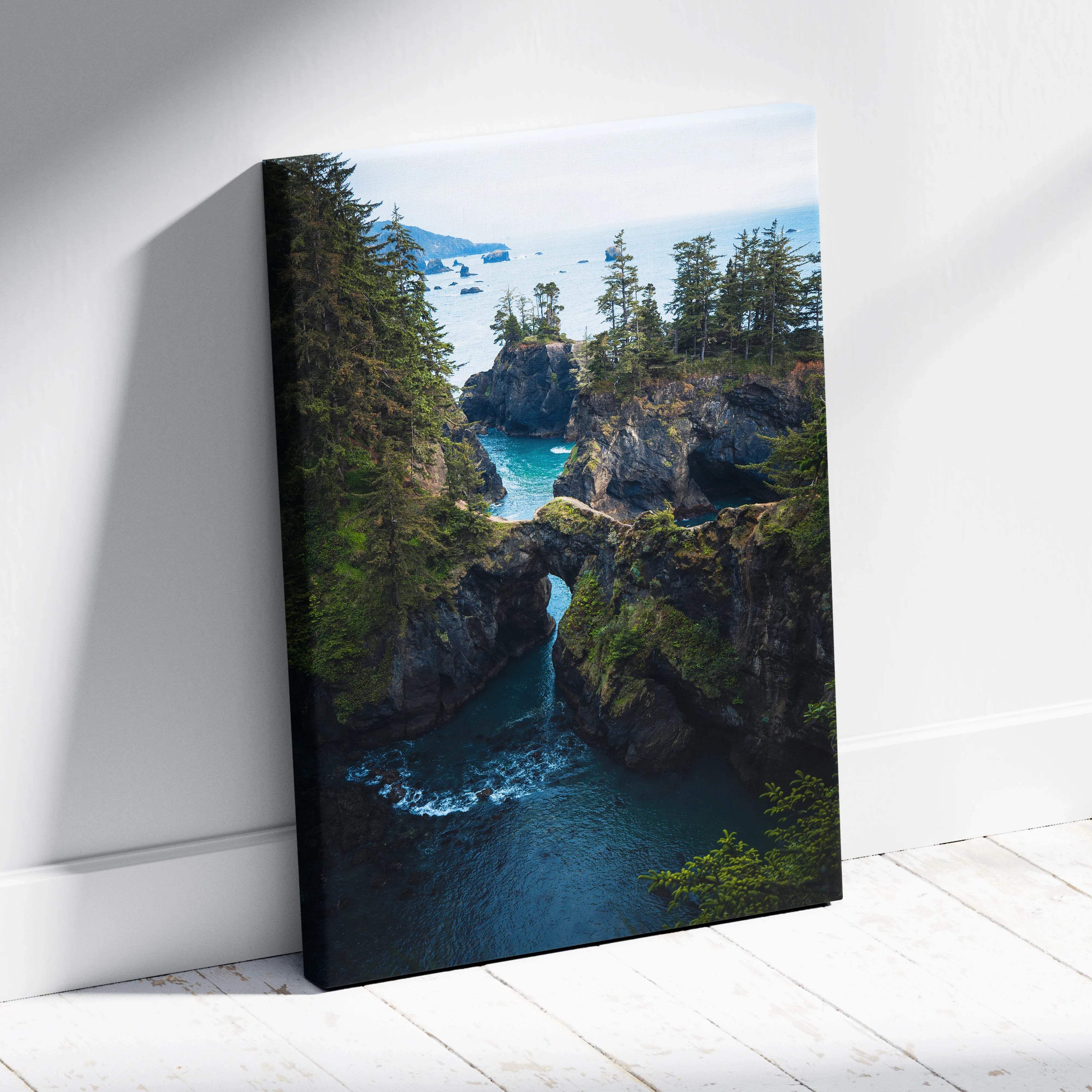 Rugged coastal cliffs with rock arch over emerald water and evergreens canvas art