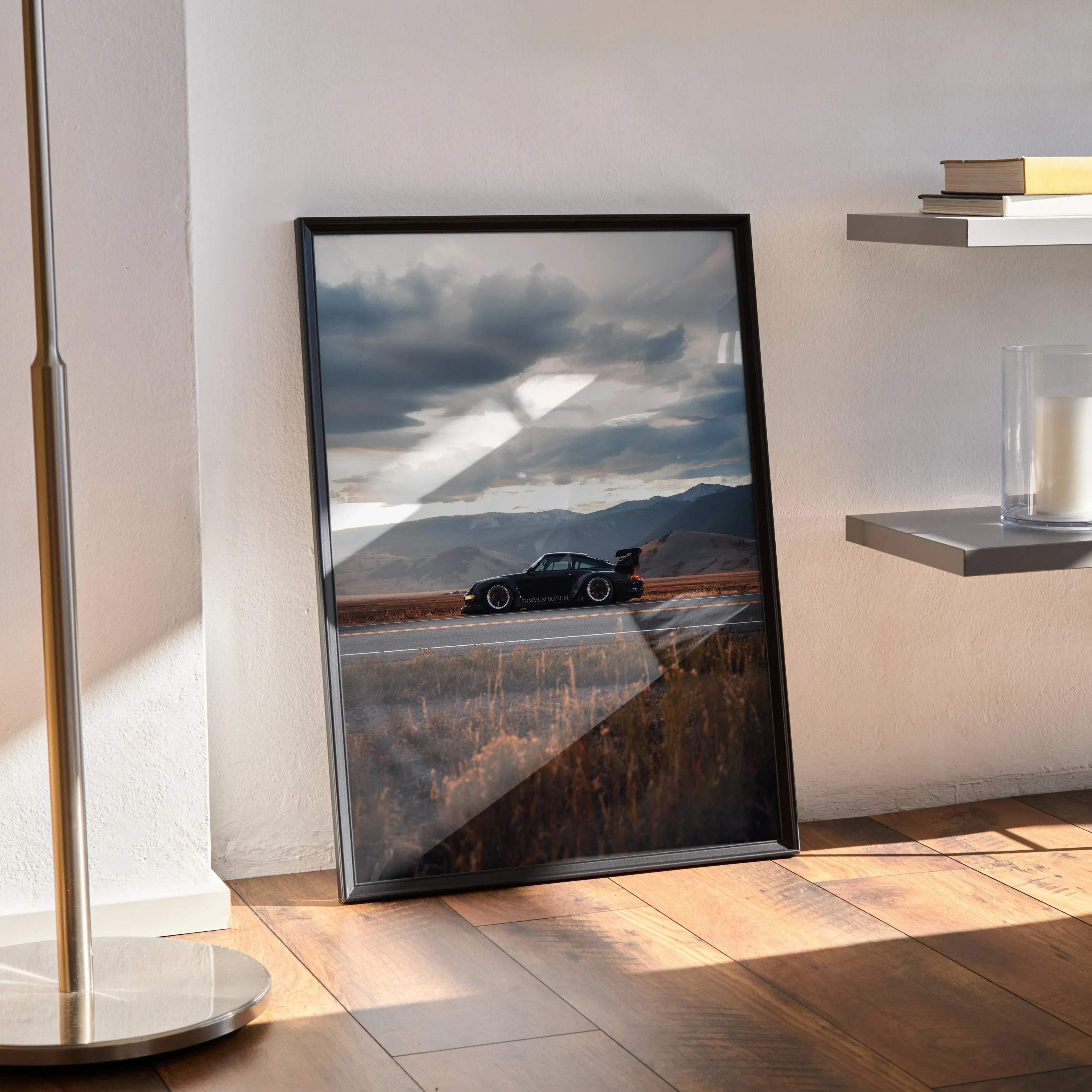 Black framed poster featuring a sleek black porsche 911 sports car speeding on a winding road under dramatic cloudy skies