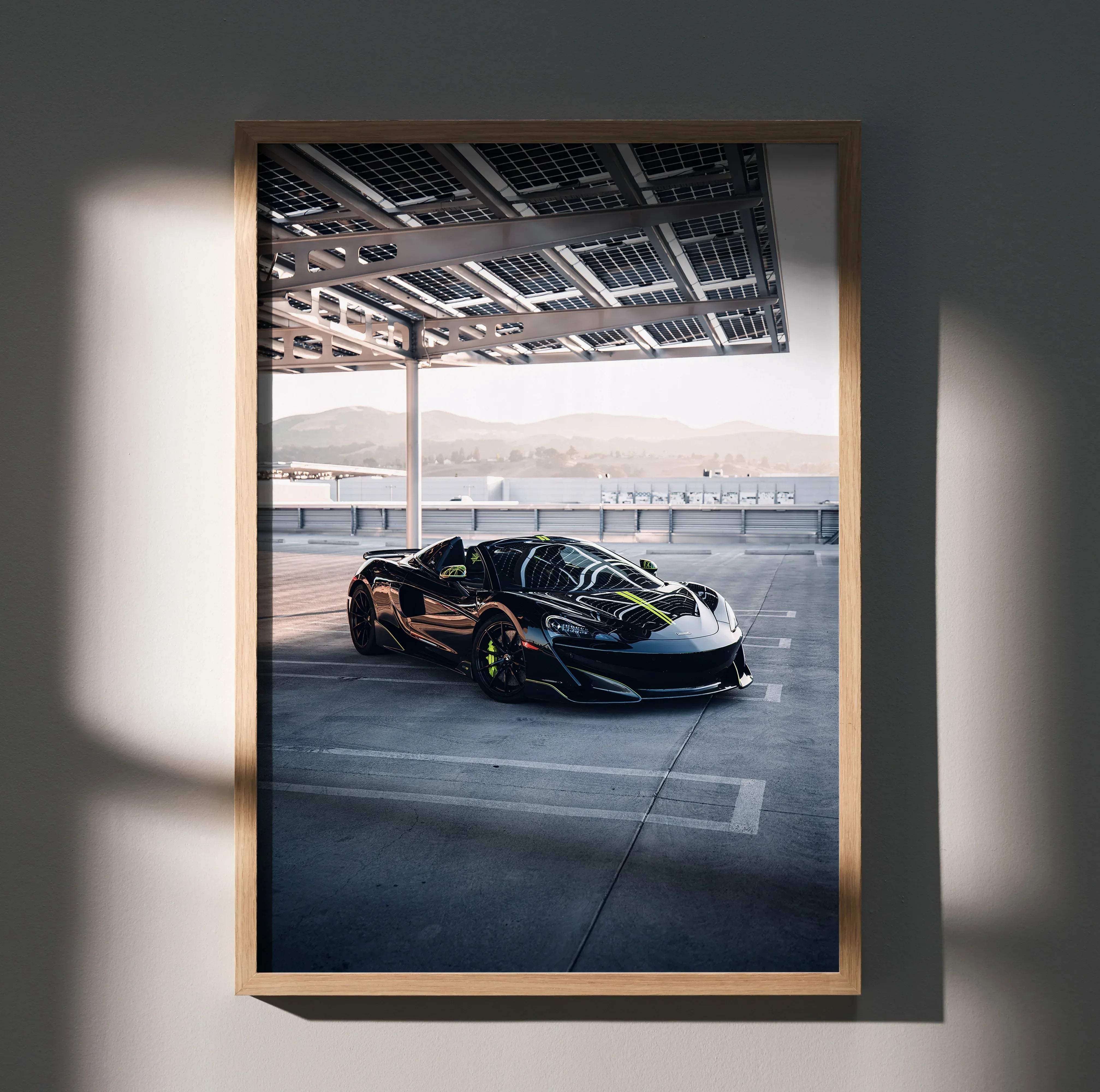 A framed photograph of a black McLaren 600LT sports car with neon green accents in a light wood frame wall decor