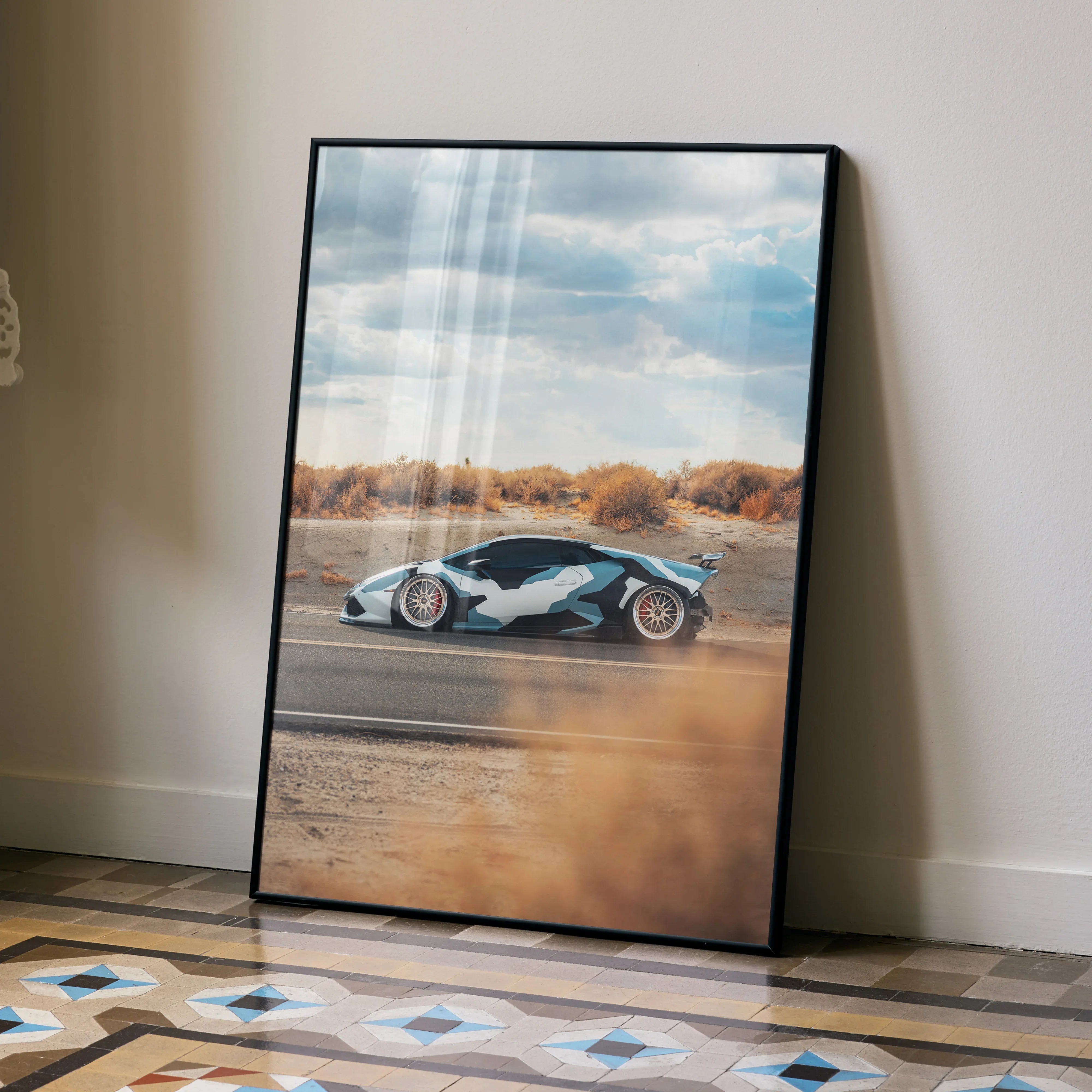 Lamborghini Huracan poster with black frame featuring dynamic side view, displayed as wall art on floor behind dried grass.