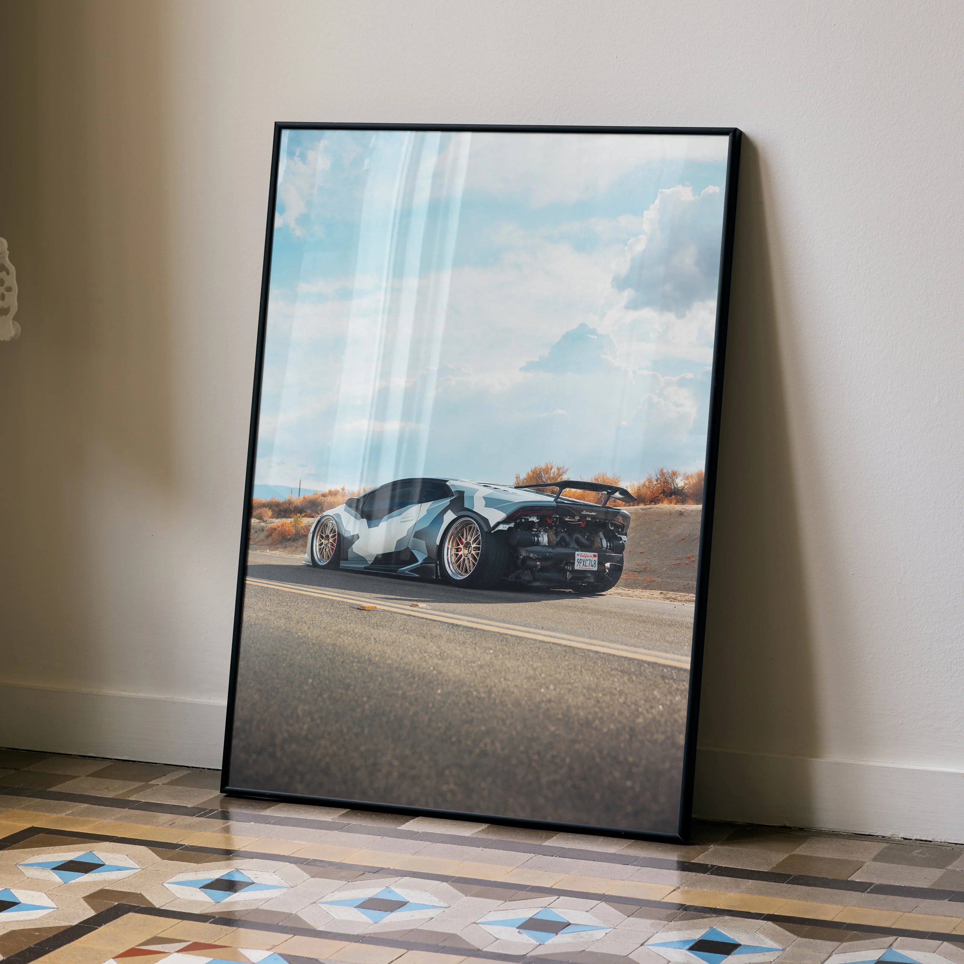 Lamborghini Huracan poster wall art with sleek black sports car and blue sky background leaning on floor.
