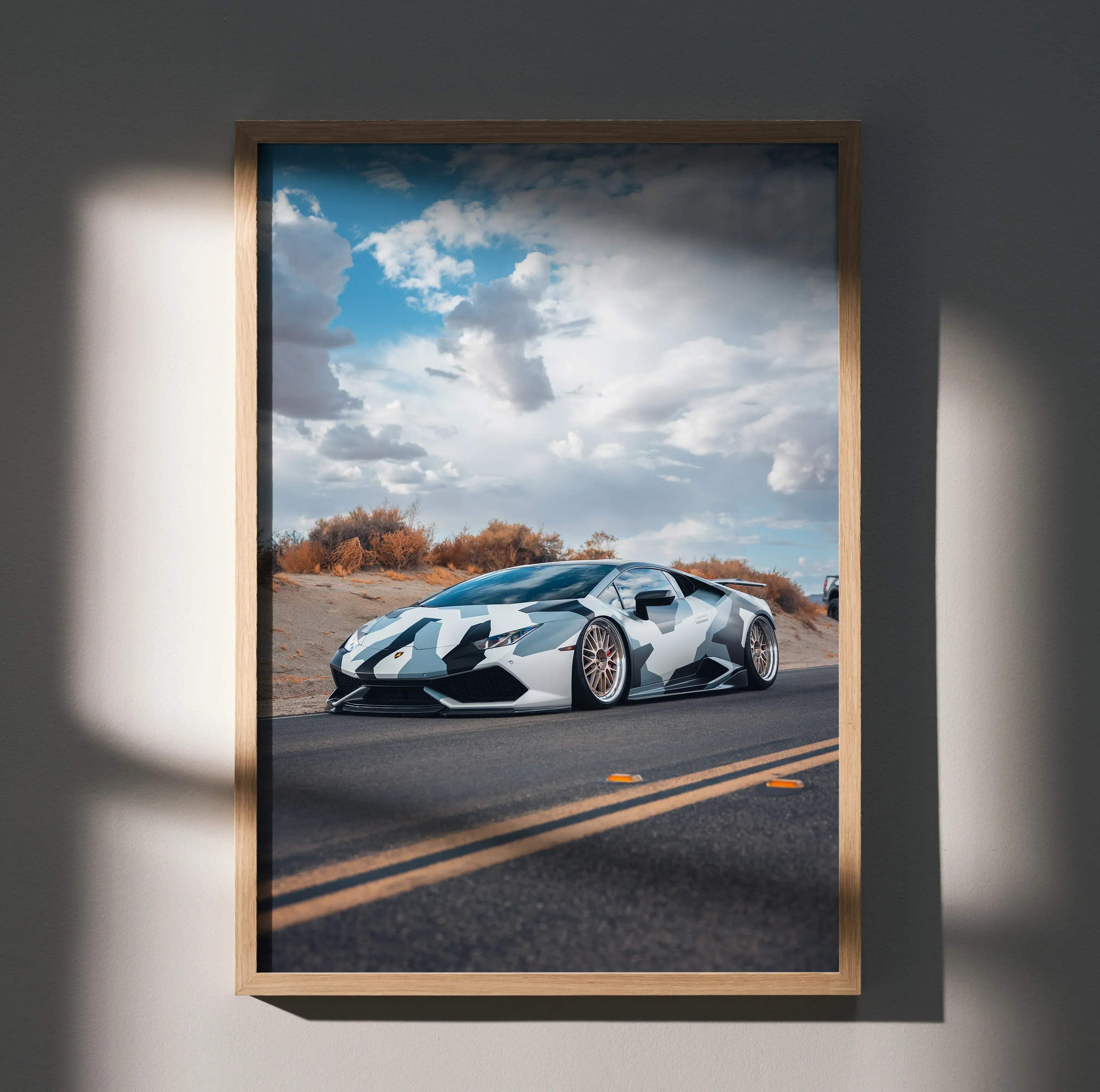 A framed poster of a white and black camouflage Lamborghini Huracan on asphalt under a cloudy sky