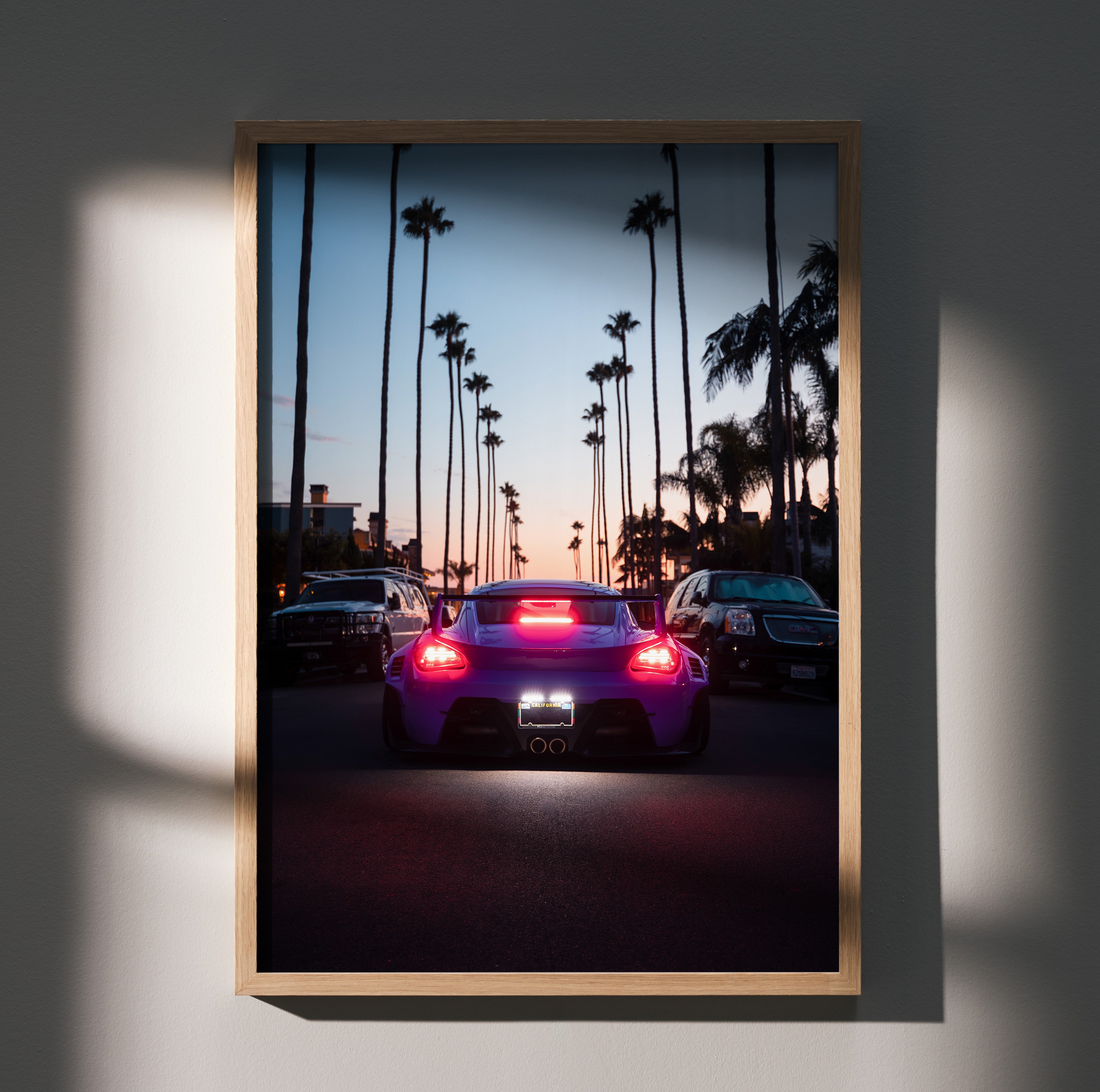 Porsche Cayman poster wall art featuring rear view of car at sunset with palm trees lining street.