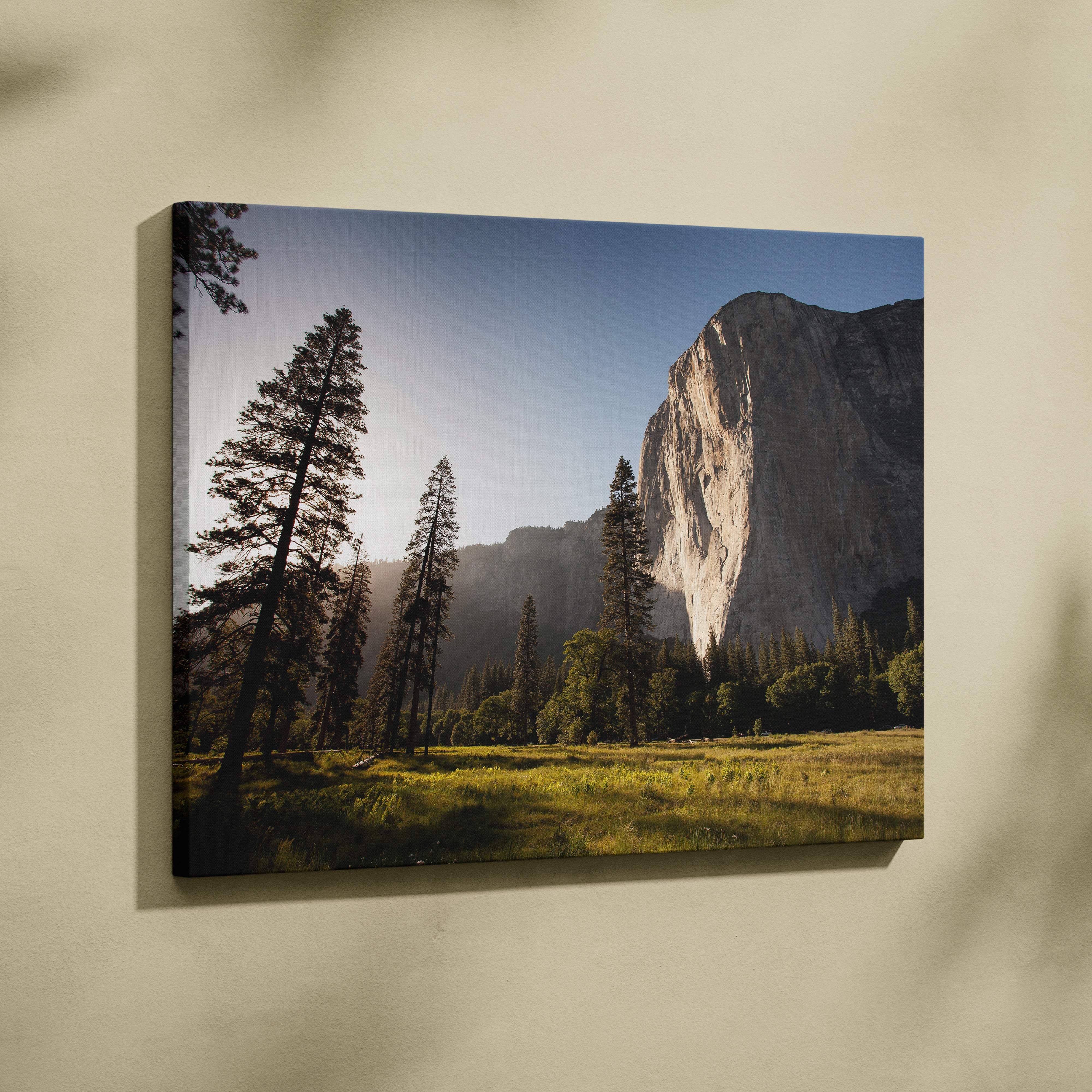 A framed canvas print of a golden sunlit yosemite cliff landscape with tall evergreen trees and rocky cliff face