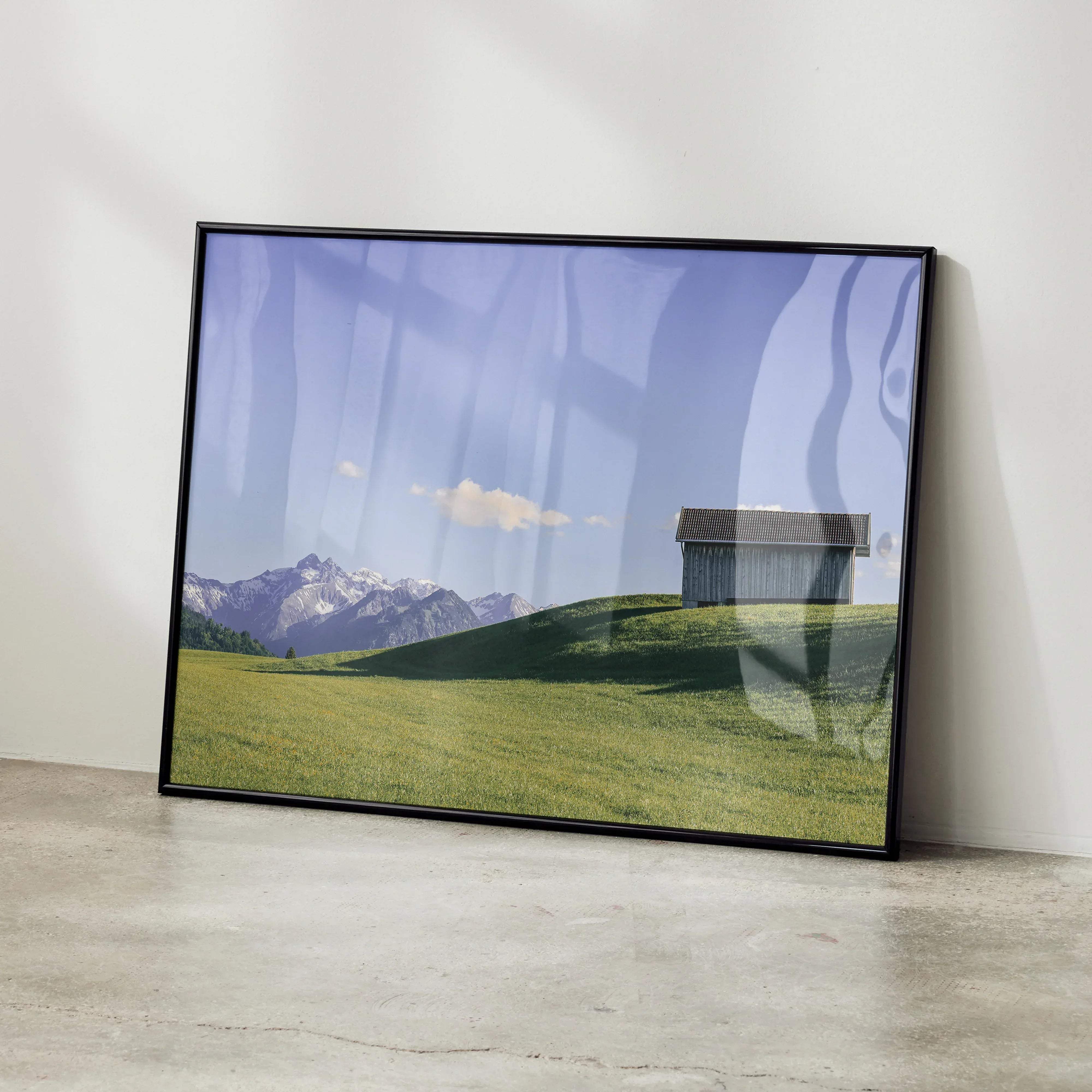 Black-framed landscape print of rustic wooden barn on green hill with snow-capped mountains for wall decor