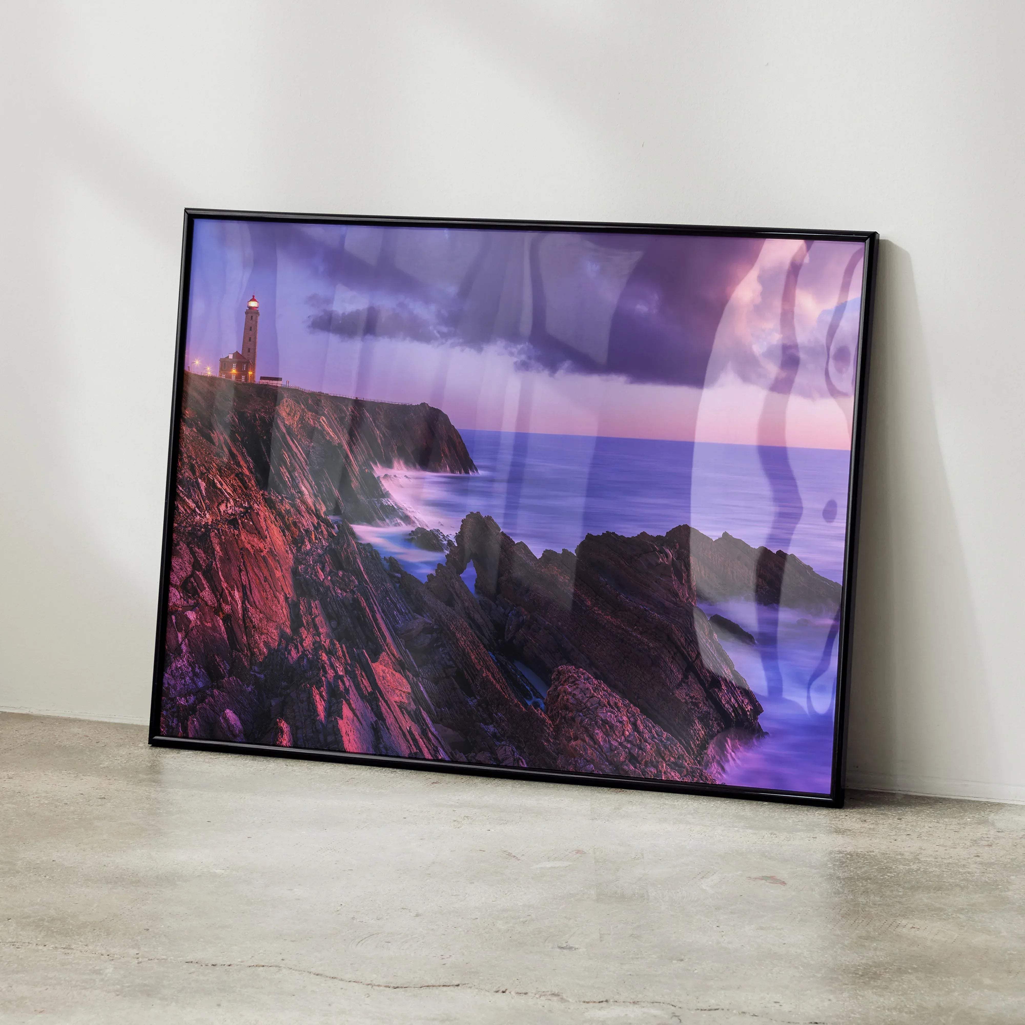 Black-framed coastal landscape print featuring a lighthouse on rugged cliffs under a vibrant purple and pink twilight sky