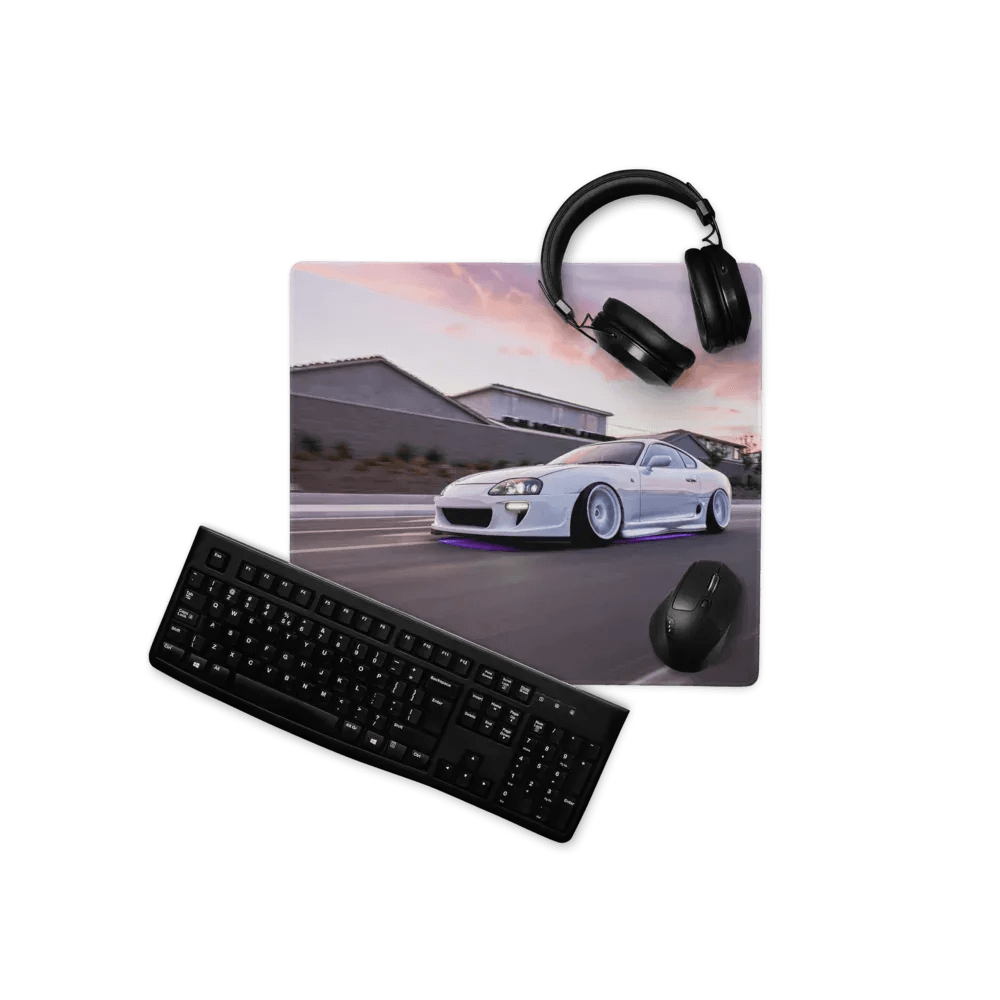 Black keyboard mouse and headphones arranged around a Toyota Supra Mk4 gaming mouse pad with white car design