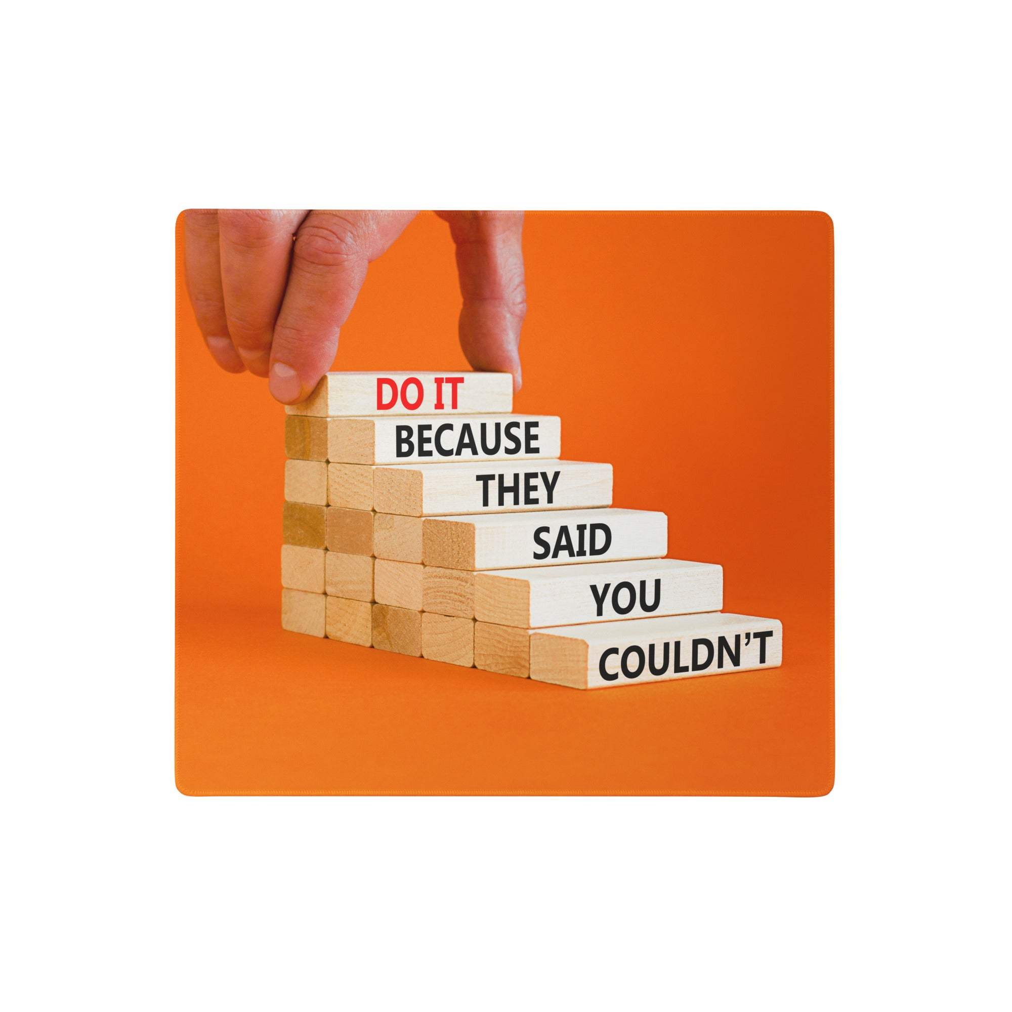 A hand places a wooden block on a staircase of engraved motivational phrases on an orange bold motivational mouse pad