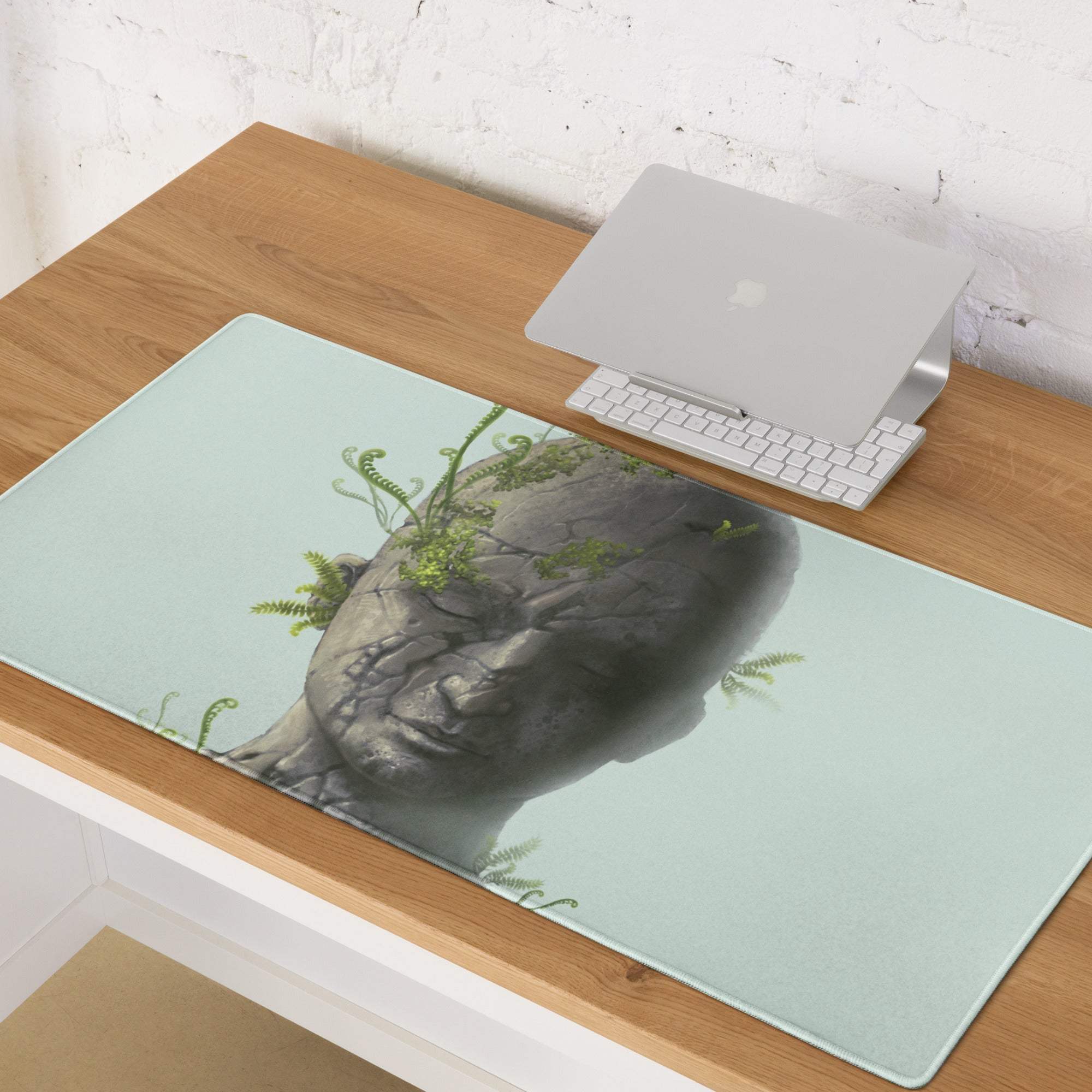 Surreal stone head desk pad in light mint green featuring a detailed stone buddha head with green ferns illustration