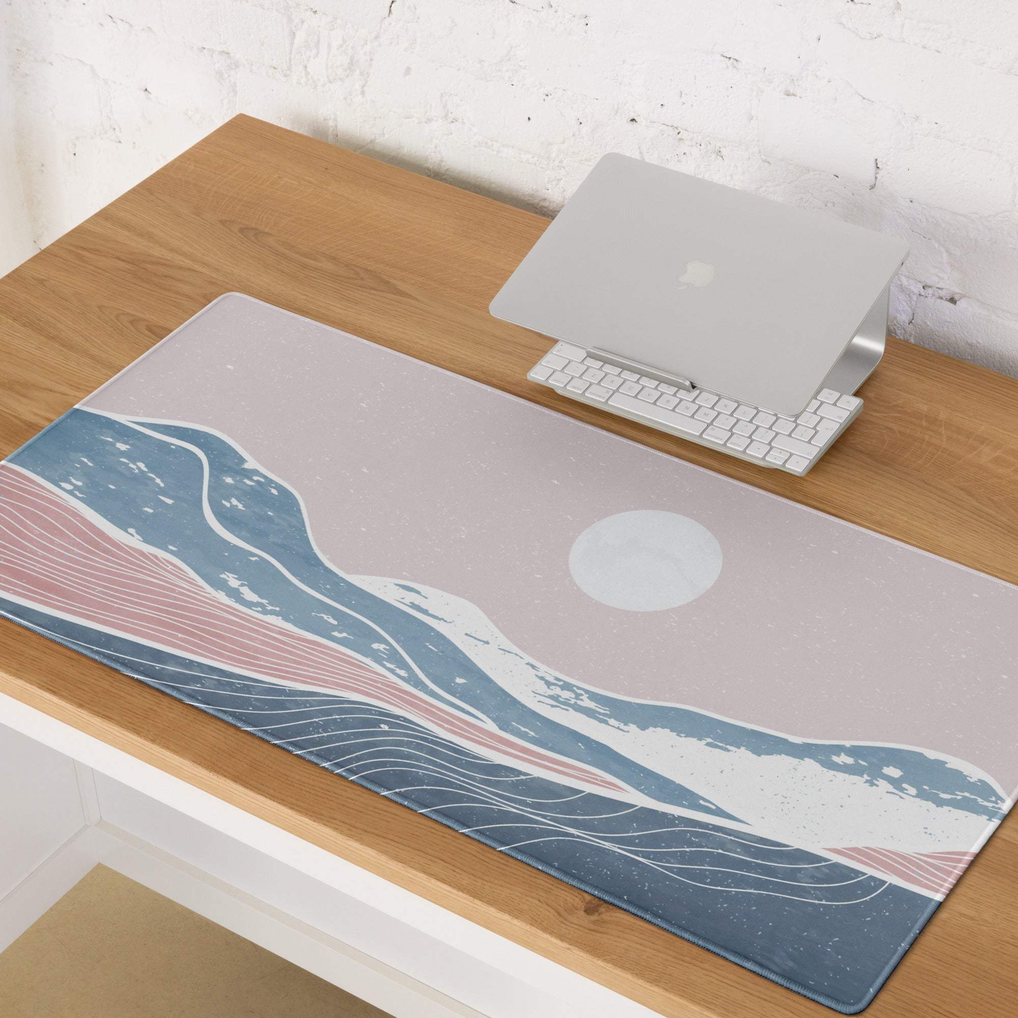 A rectangular soft-touch pastel ocean wave desk pad with blue and pink waves on a muted gray background
