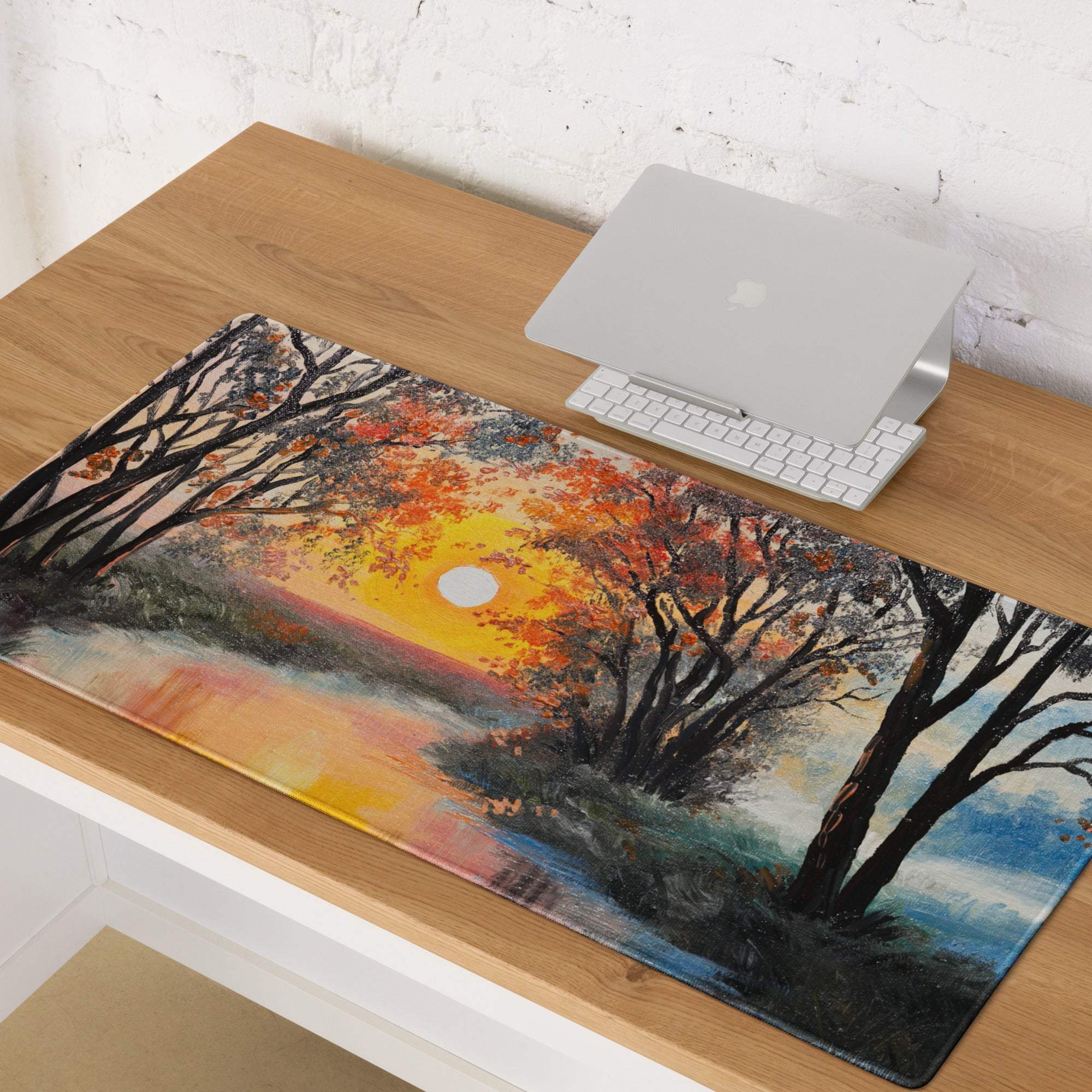 A rectangular glossy desk pad featuring a vibrant orange and yellow forest sunset oil painting over water