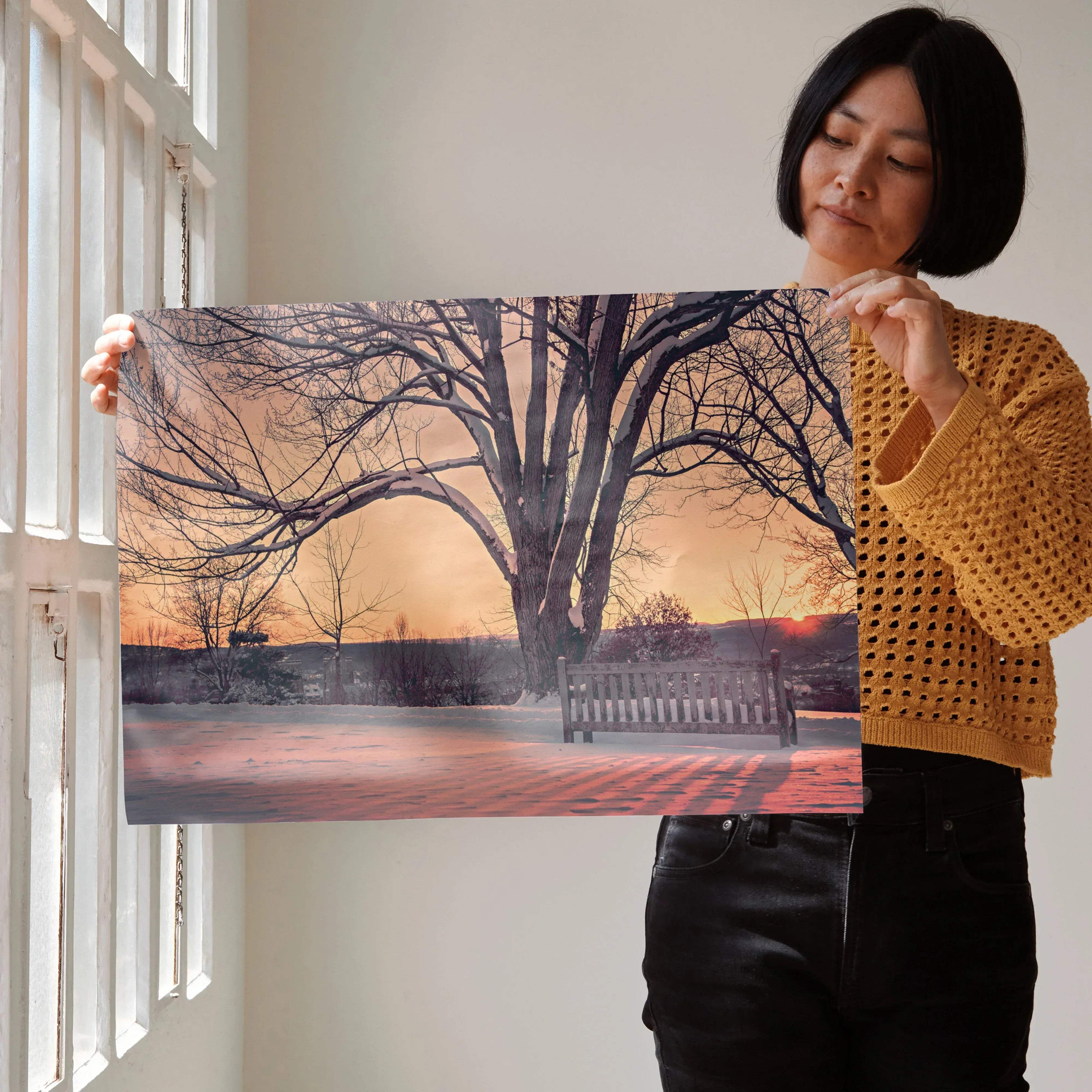 Rectangular framed print of a solitary tree with bare branches against an orange sunset sky and snow-covered park bench