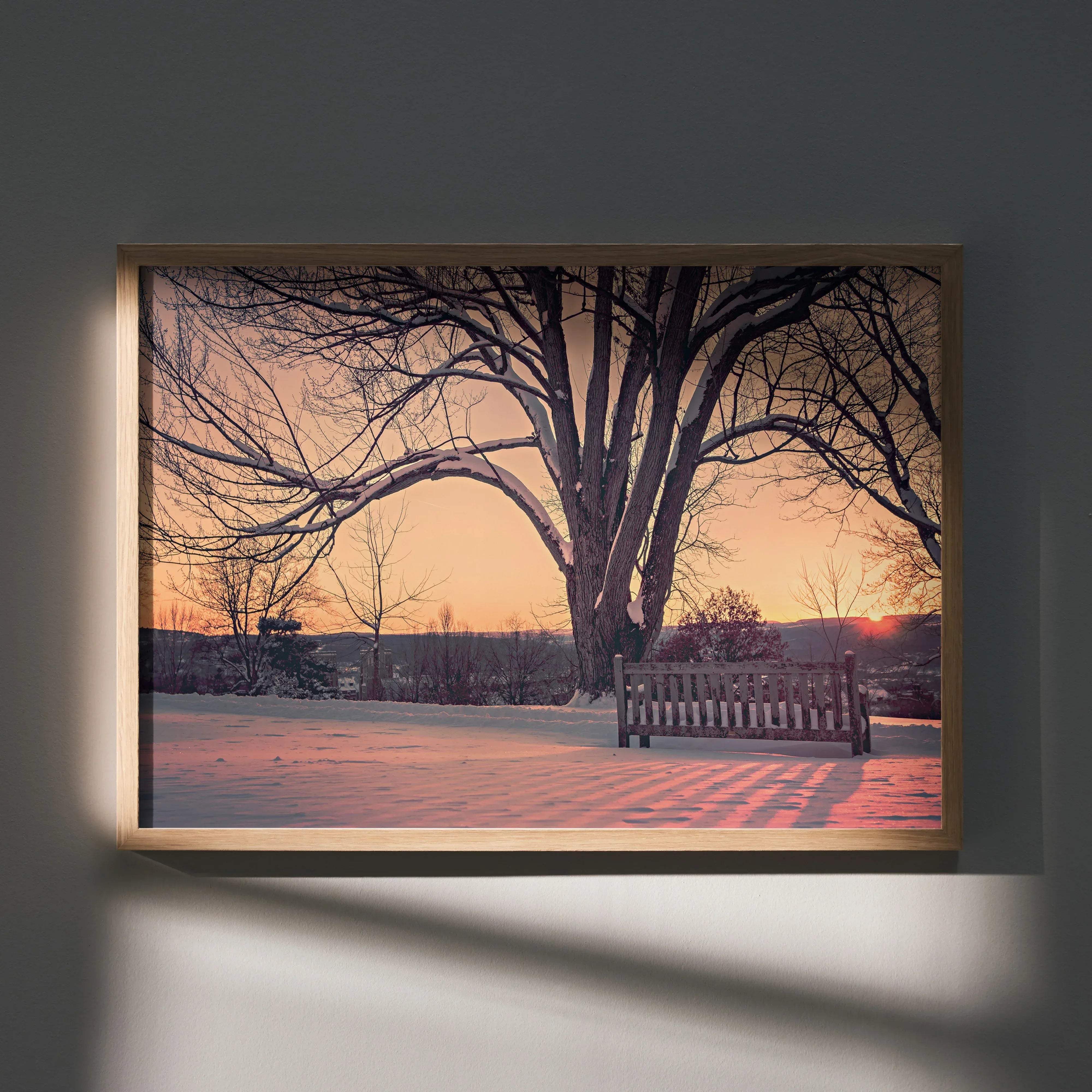 A framed nature art print poster of a serene snowy park scene with bare trees and a wooden bench at sunset