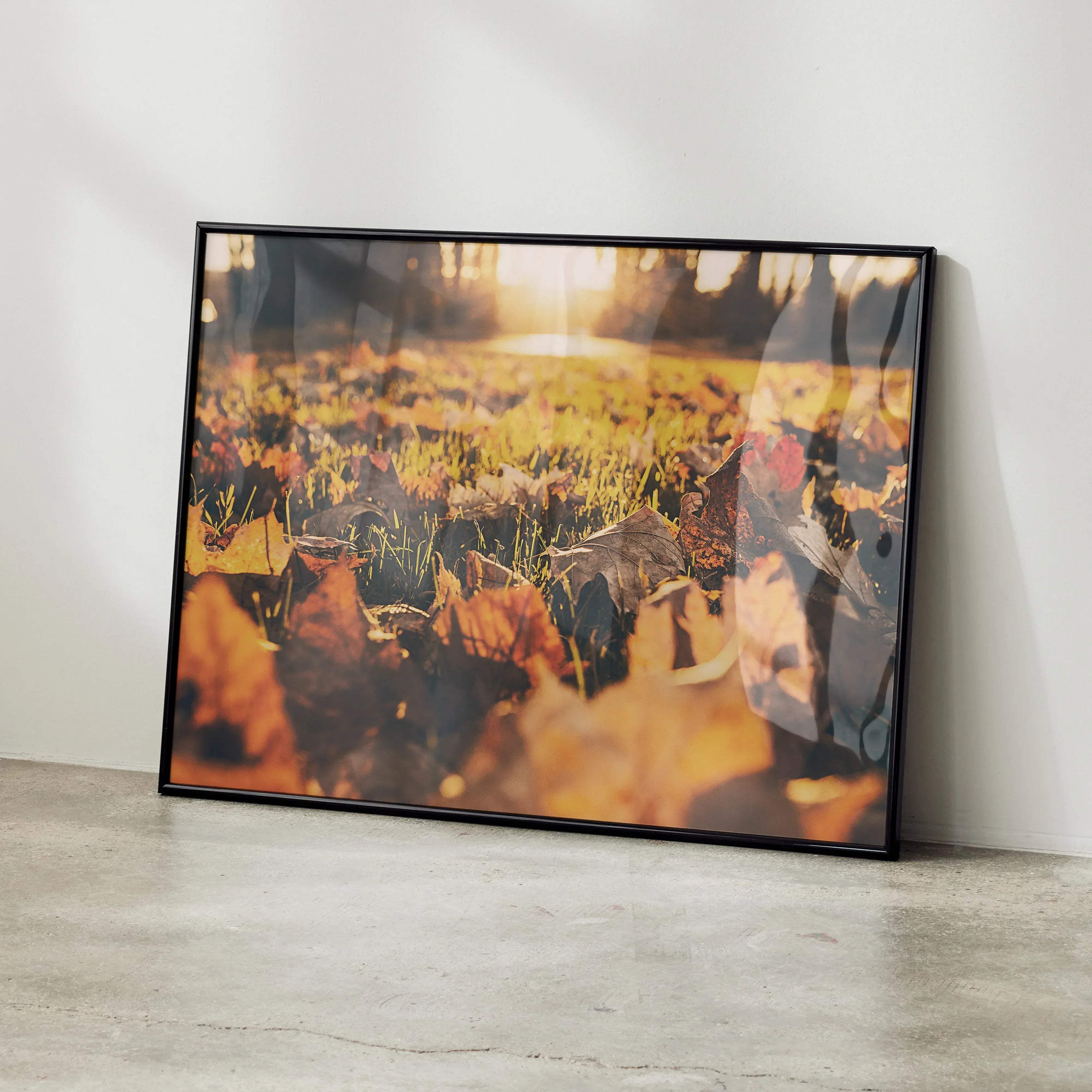 Black-framed wall art featuring a warm golden-hued photograph of vibrant autumn leaves scattered on grass