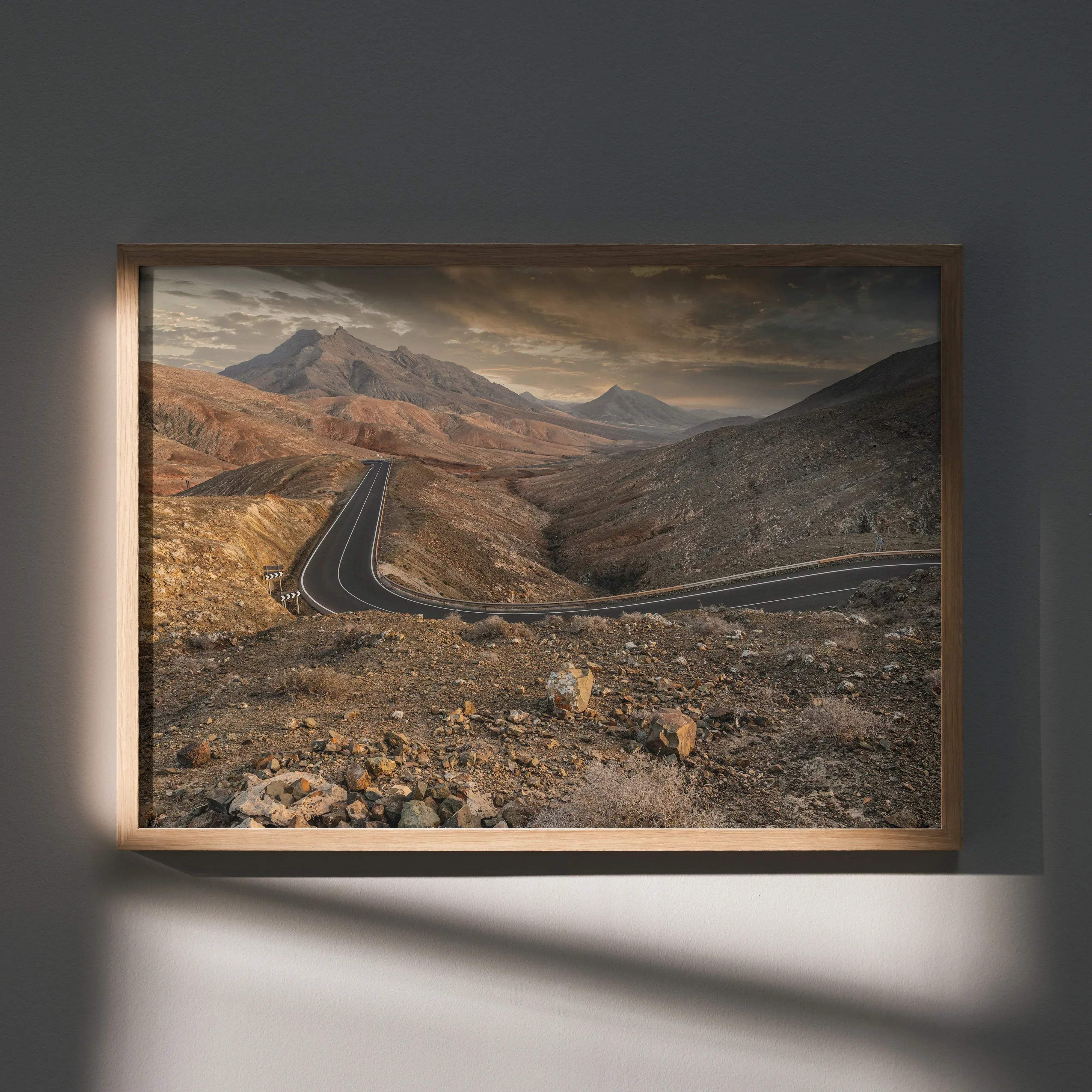 A framed stunning mountains sunset wall art poster print featuring a winding asphalt road through rugged arid mountains