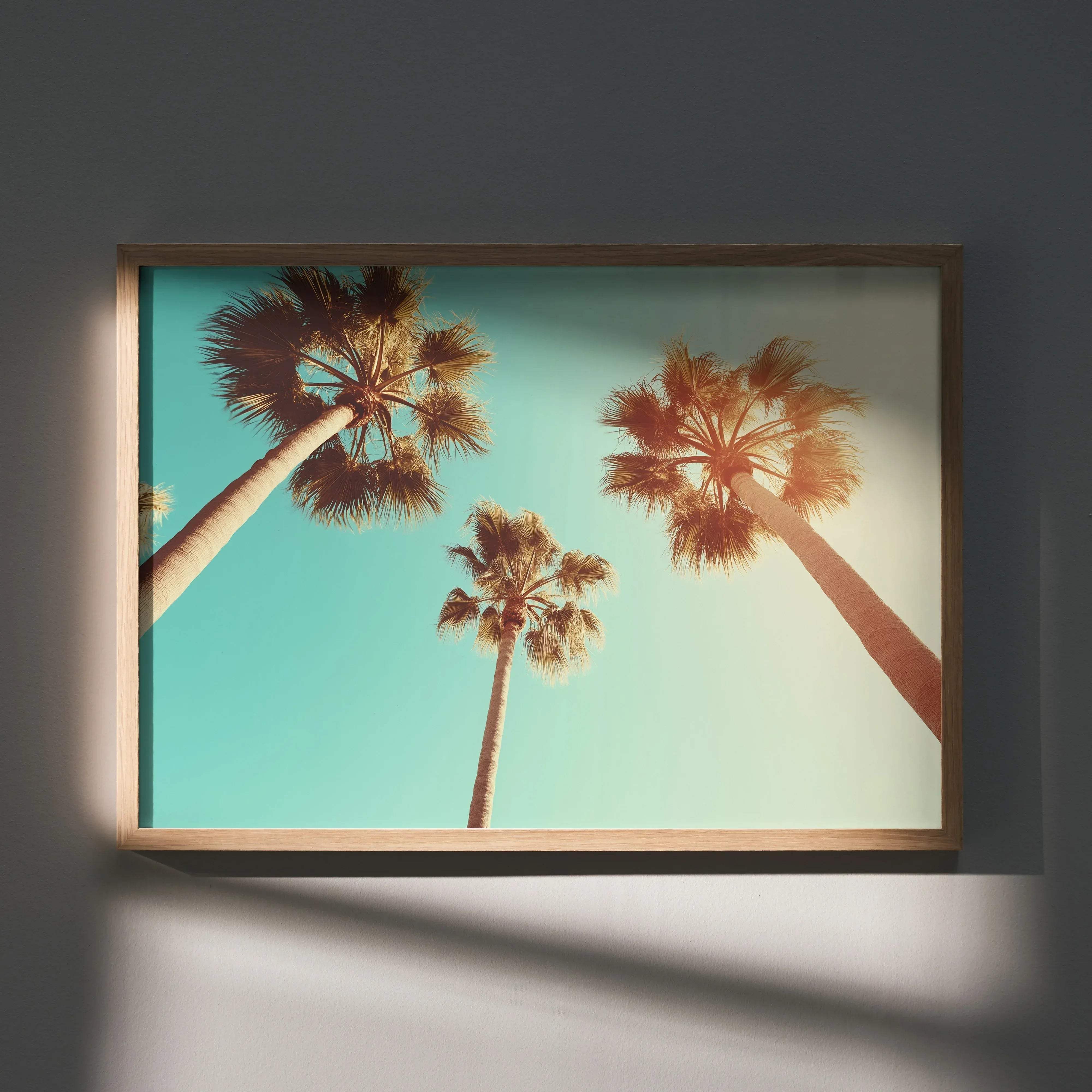 A framed serene beach digital art print featuring three palm trees against a vibrant turquoise sky in light wood frame