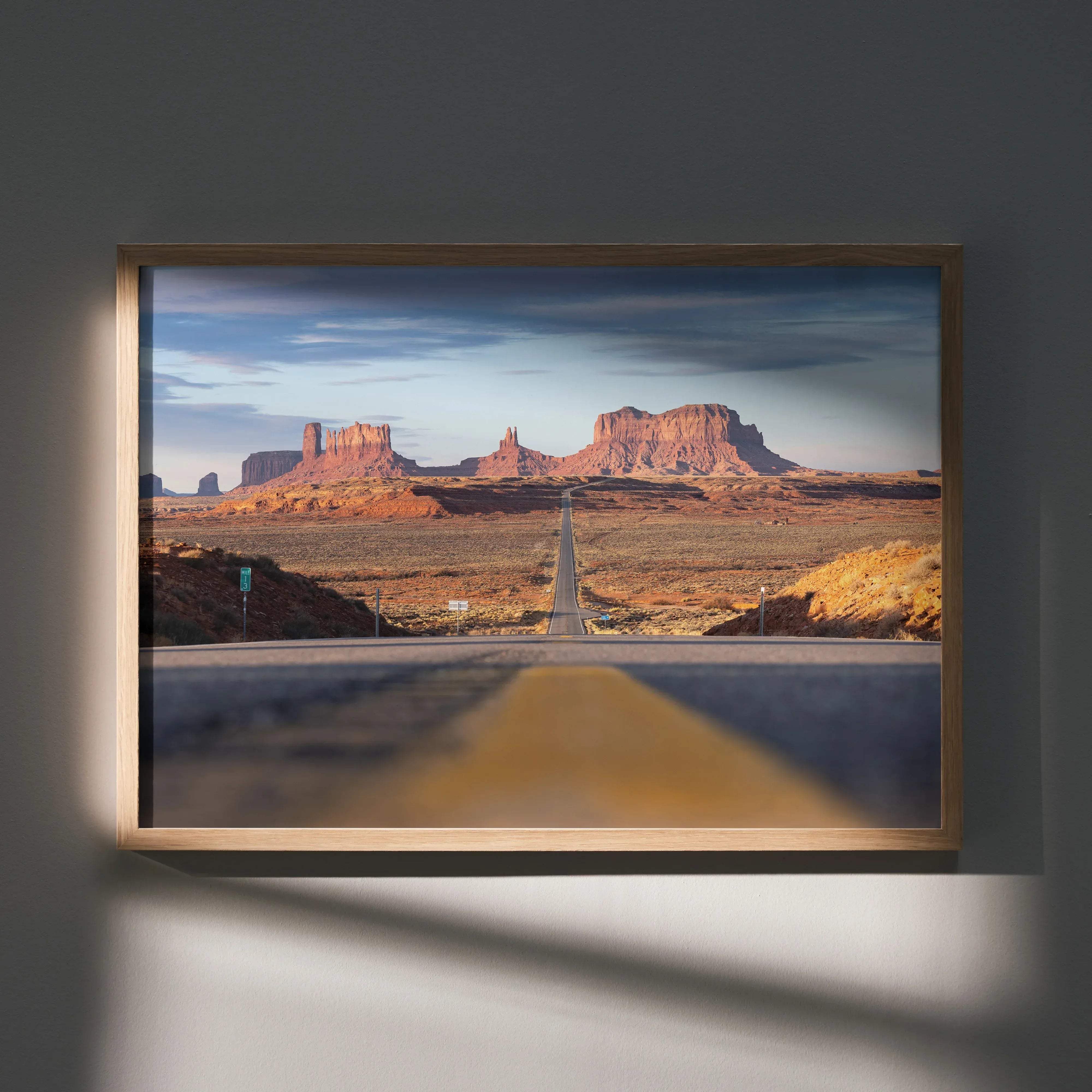 A framed majestic mountain landscape wall art poster featuring red rock formations and a long desert road in a light wood frame