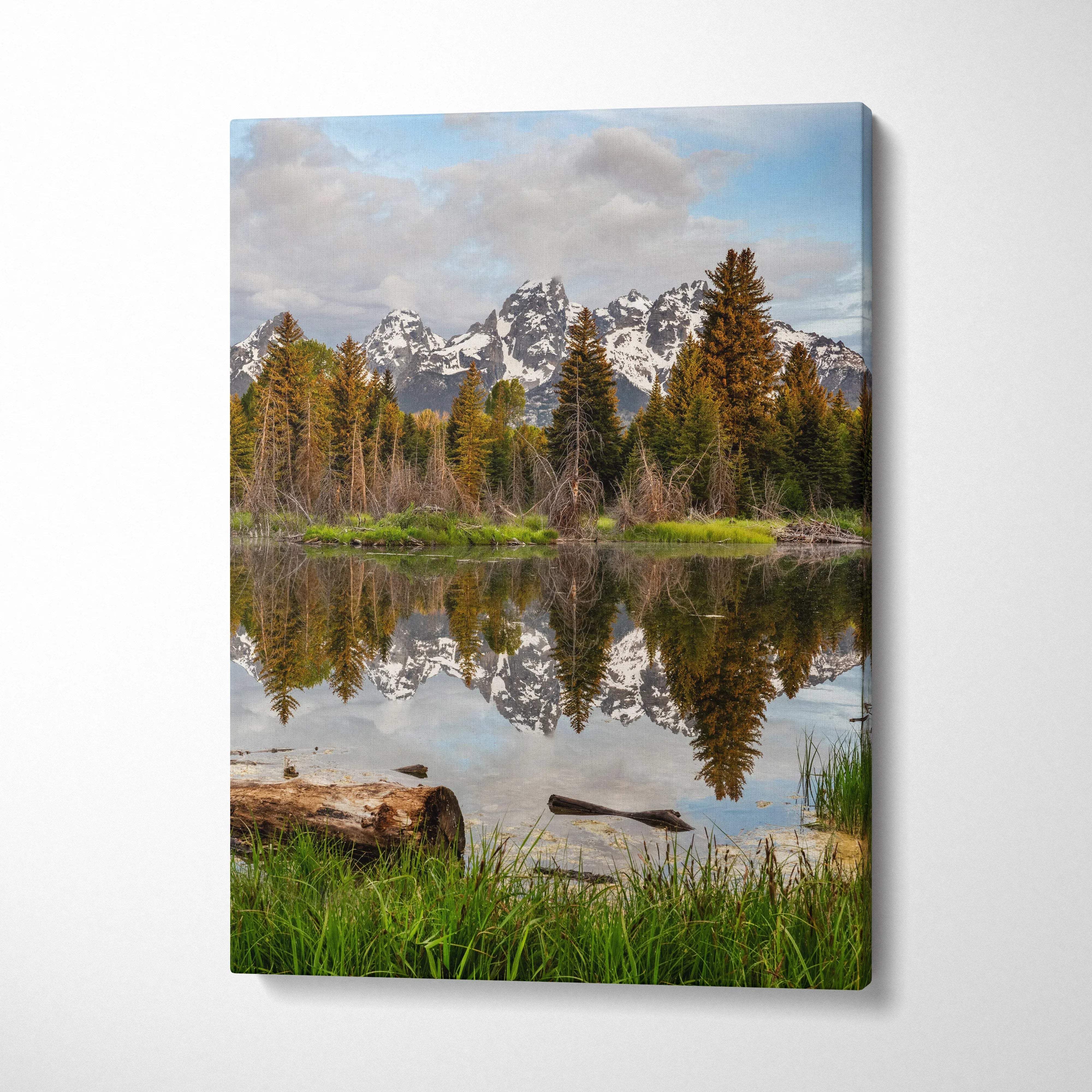 Vertical canvas wall art featuring snow-capped mountains reflected in a tranquil lake with pine trees and grassy foreground.