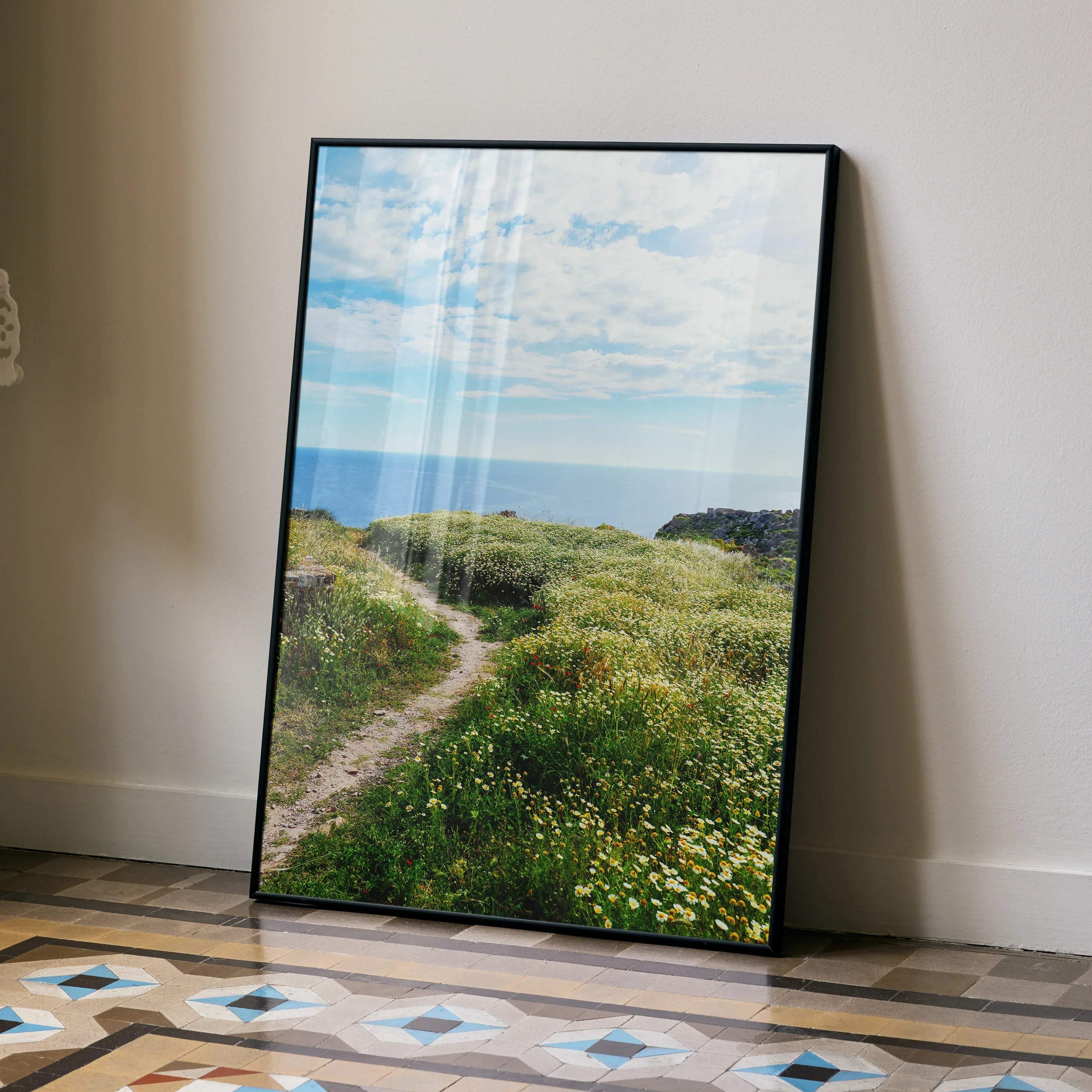 Black-framed vibrant floral nature wall art poster featuring a sunlit coastal path with green grass and yellow wildflowers