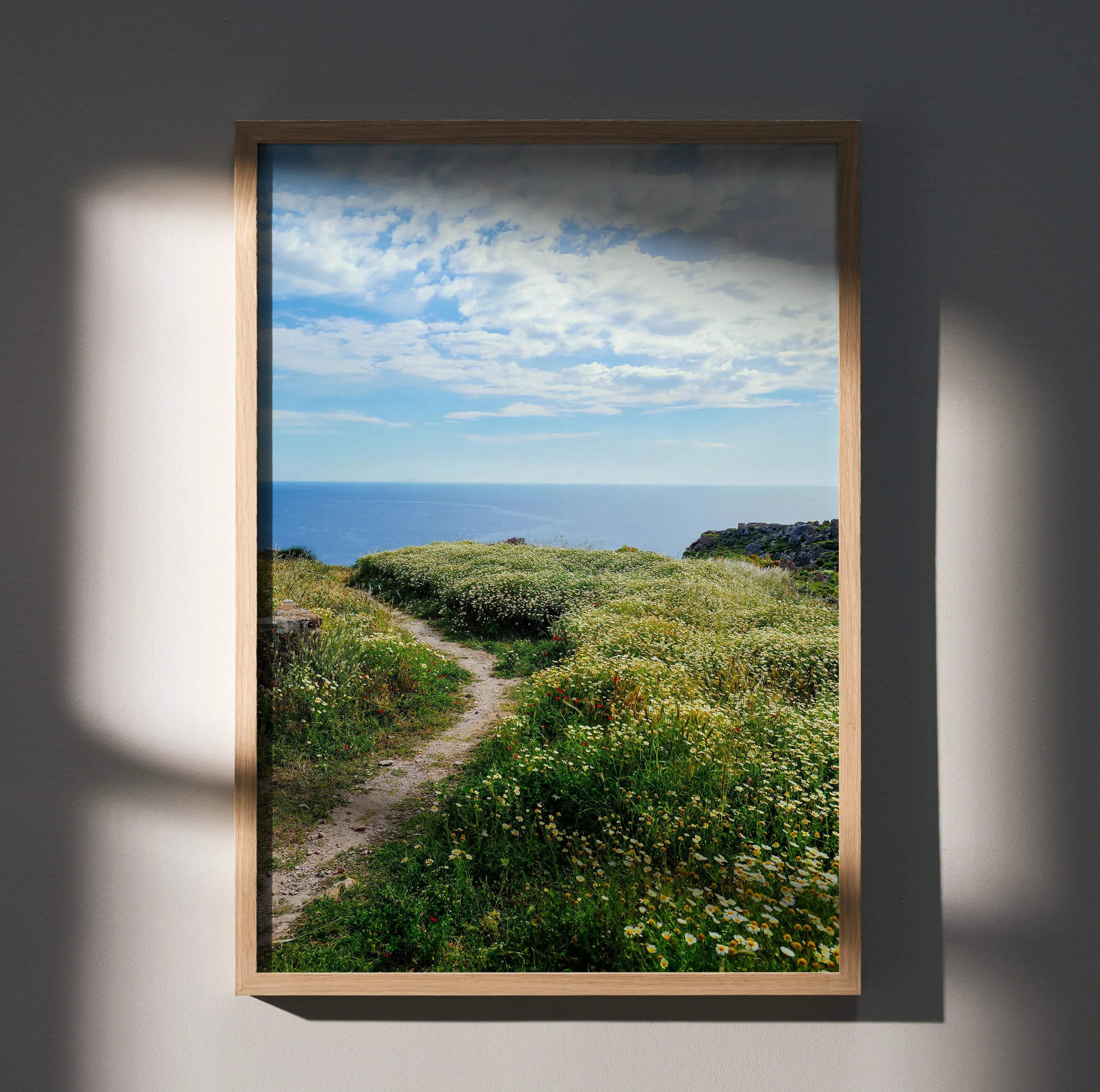 A framed vibrant floral nature wall art poster featuring a coastal path through green wildflowers under a cloudy sky