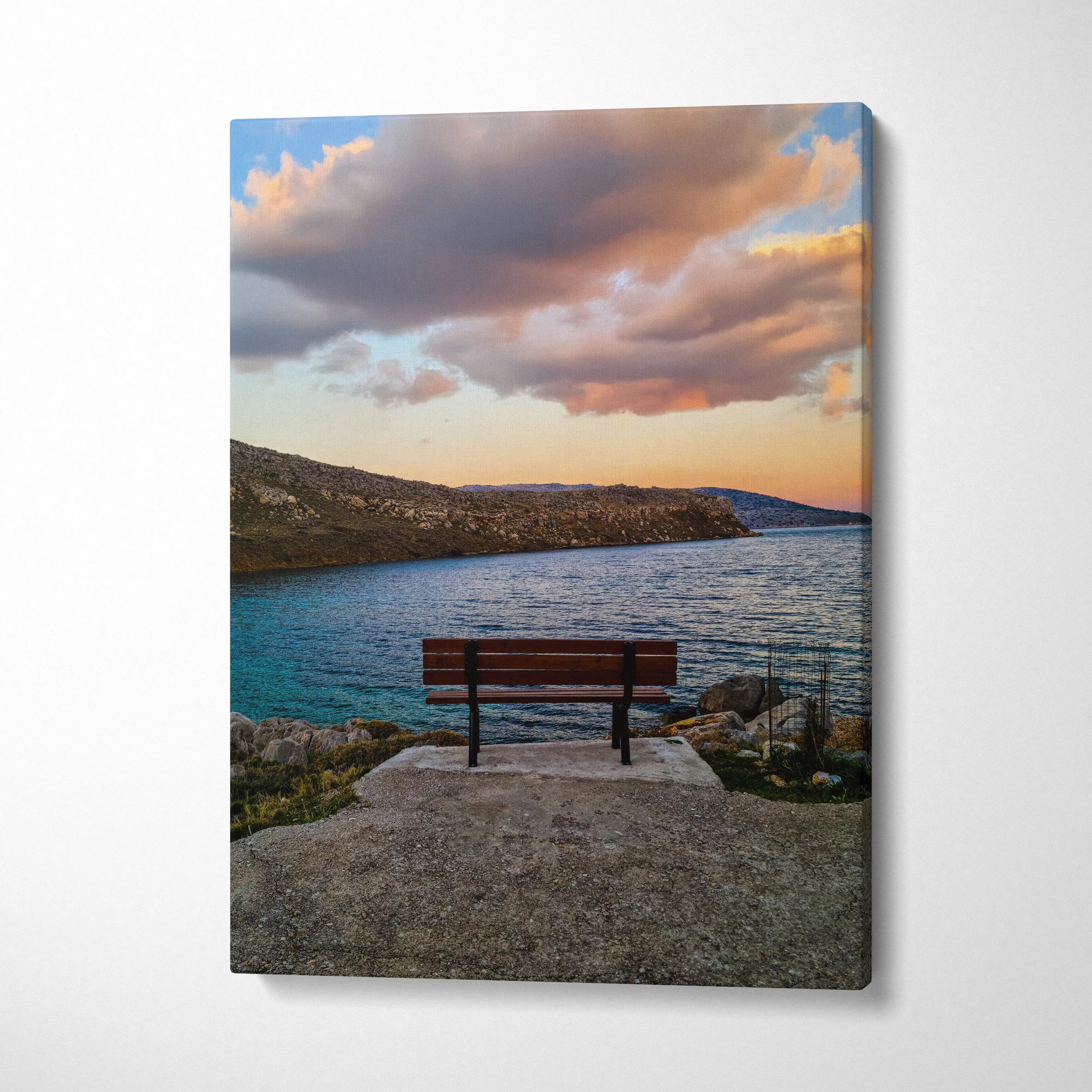 Canvas wall art featuring a vivid sunset over a rocky coastline with a bench in the foreground.
