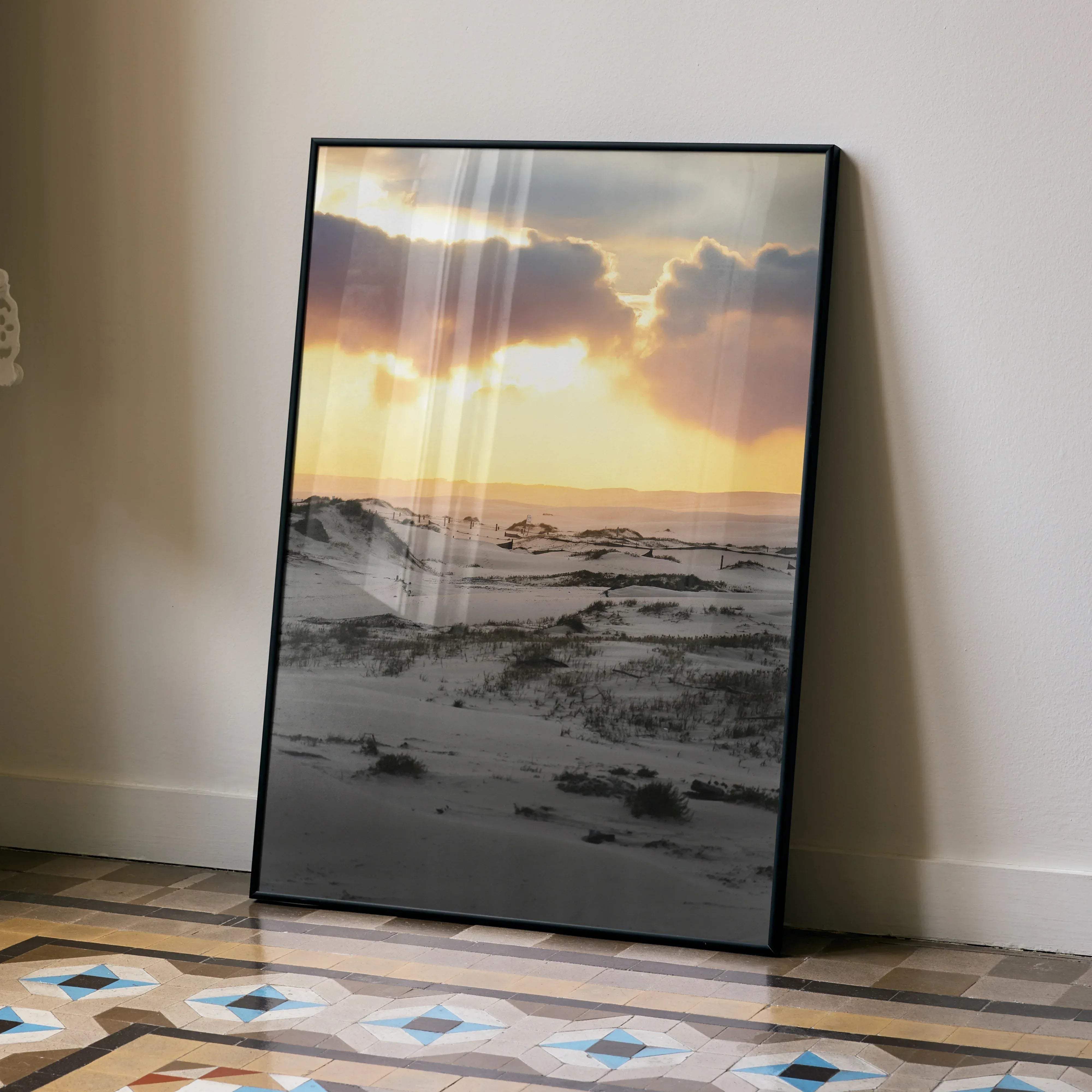 Black-framed stunning snow and sunset art print wall decor featuring sunlit dune with orange and yellow skies above gray sands