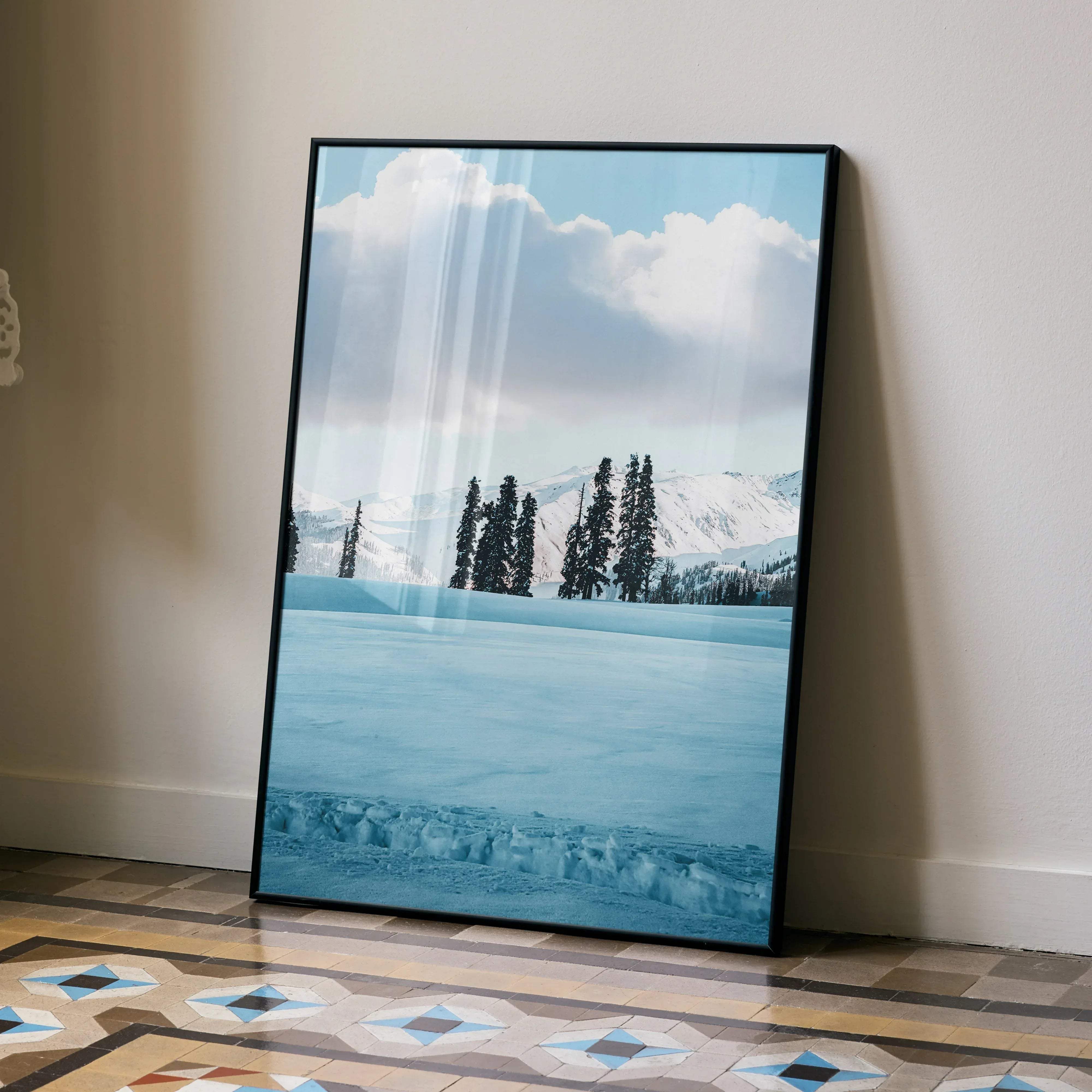 A framed vertical winter landscape print with a black frame showcasing snow-capped mountains and evergreen trees