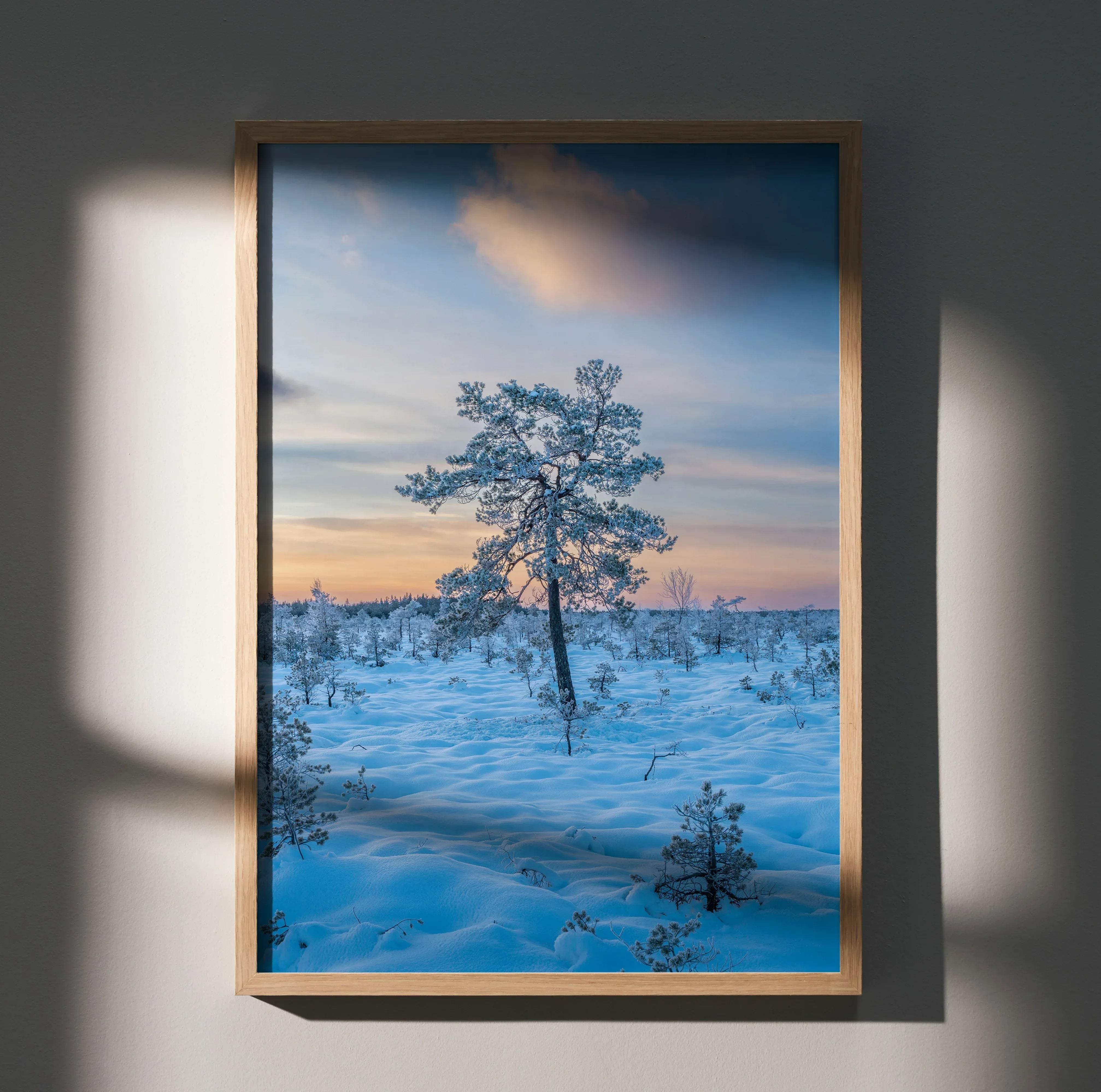 A framed serene snowy landscape winter art print poster featuring a solitary snow-covered tree in a light wood frame