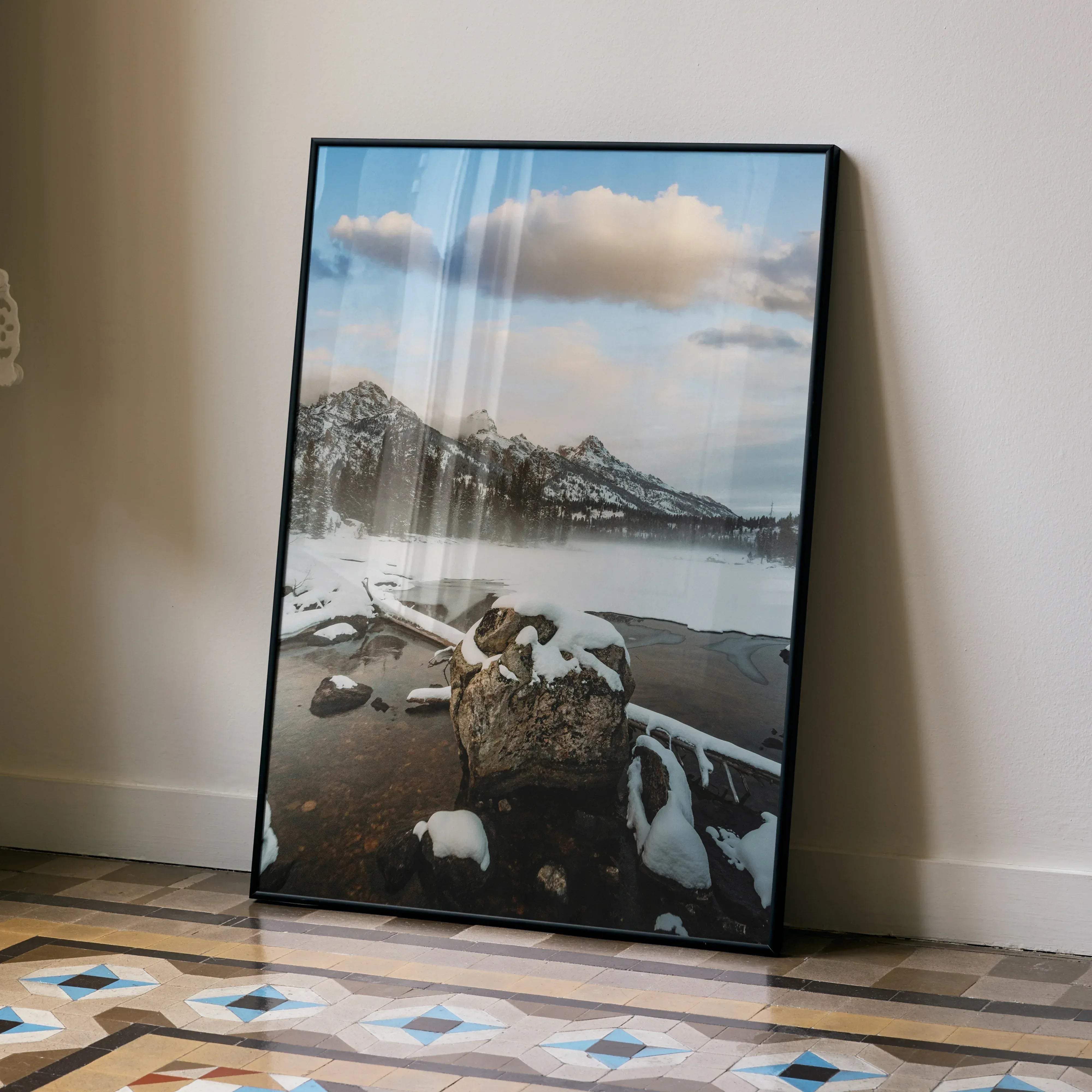 Black-framed vertical photograph poster of majestic snowy mountains and a serene lake with rocks in the foreground