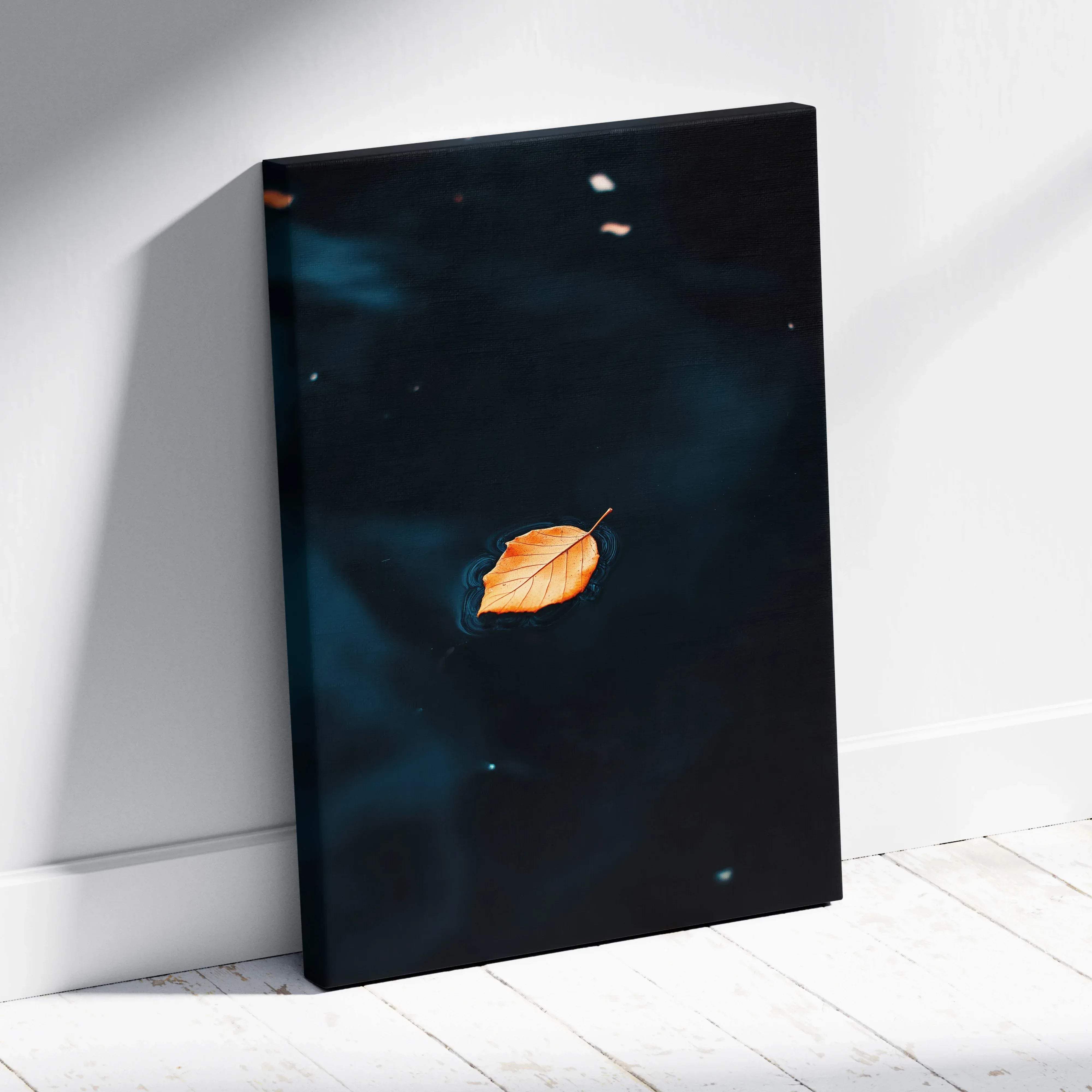 A minimalist canvas wall art featuring a golden orange leaf floating on moody dark blue water with light reflections