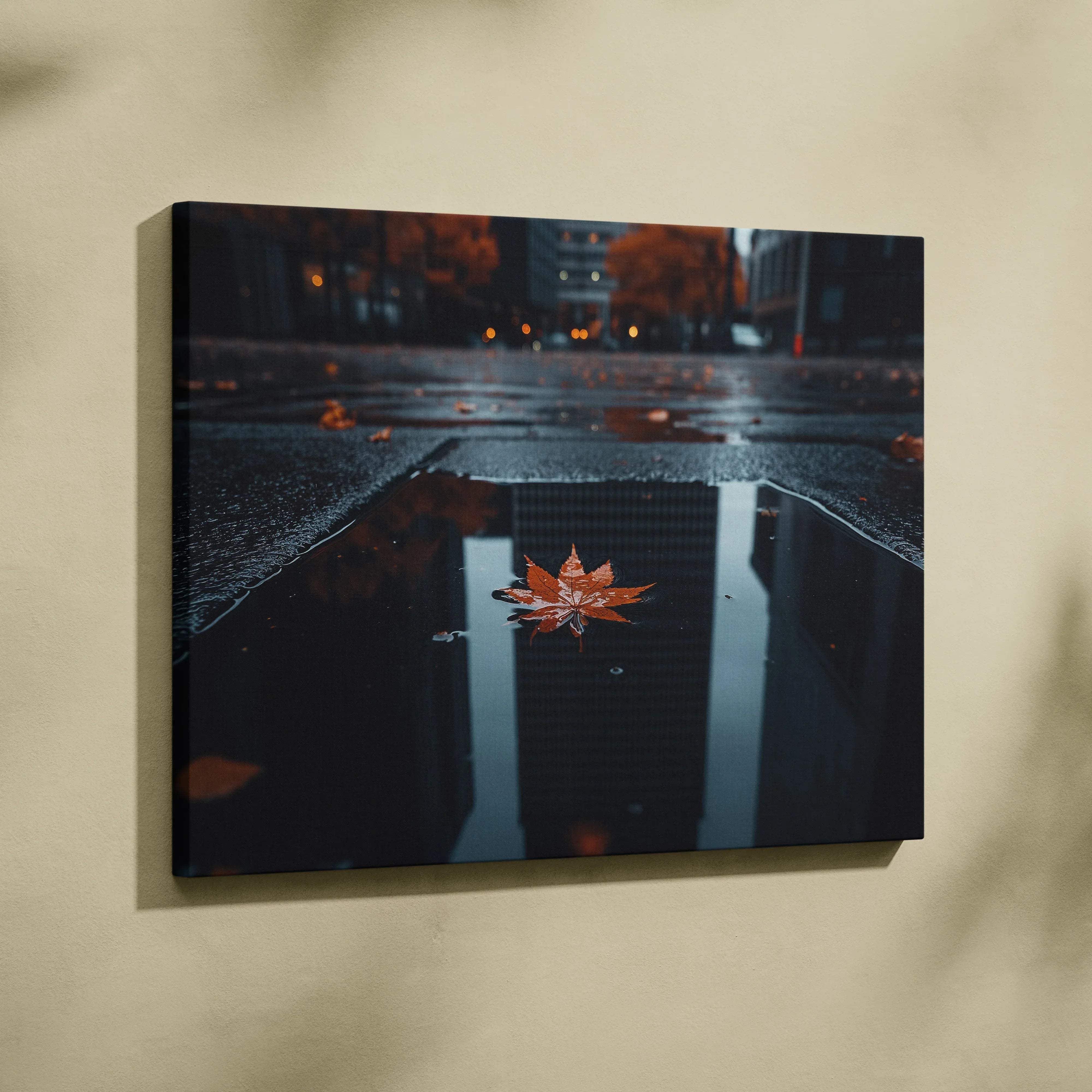 A minimalist canvas wall art of an orange maple leaf floating in a dark puddle with blurred city lights reflection