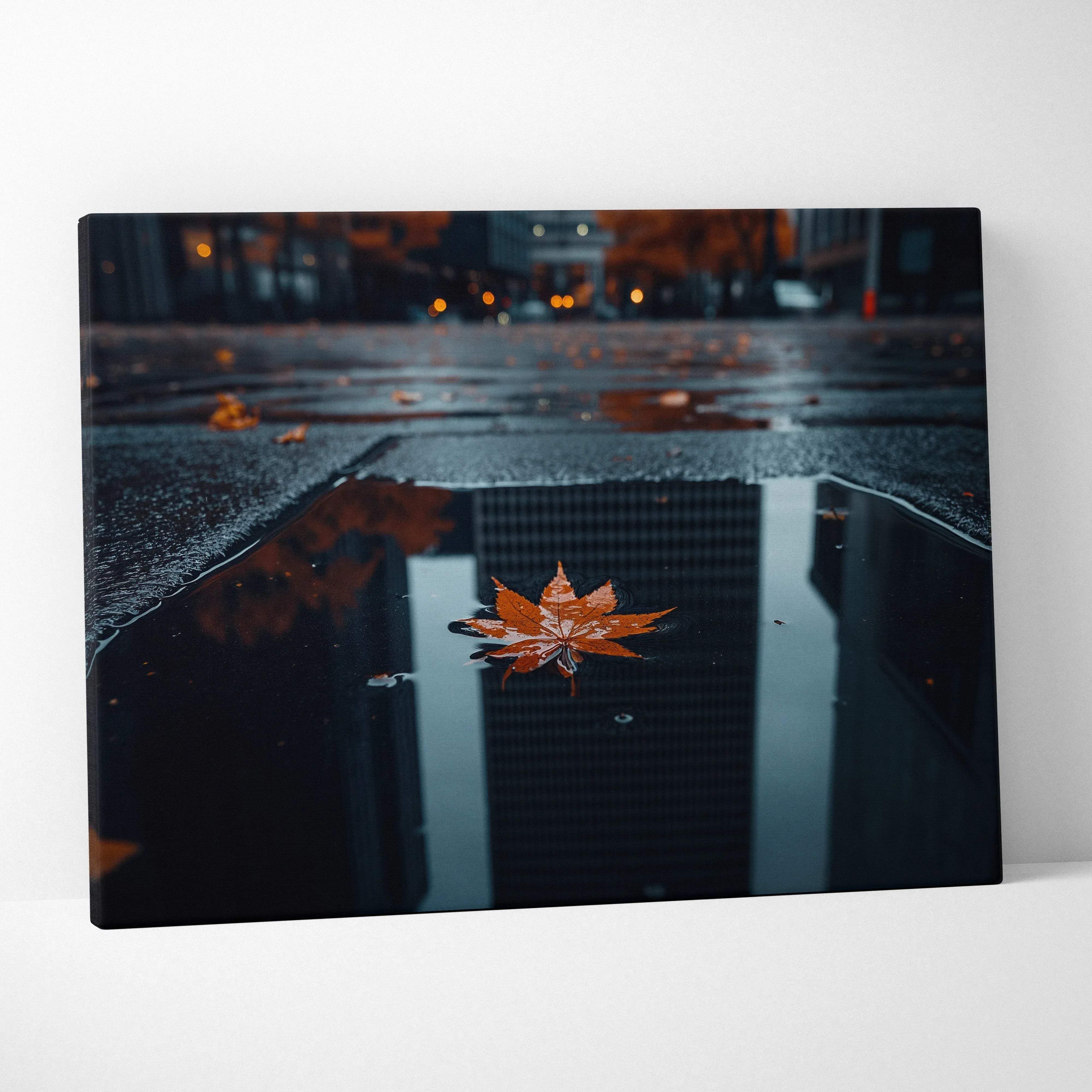 A canvas print featuring a vibrant orange maple leaf floating in a reflective city puddle with golden earthy tones