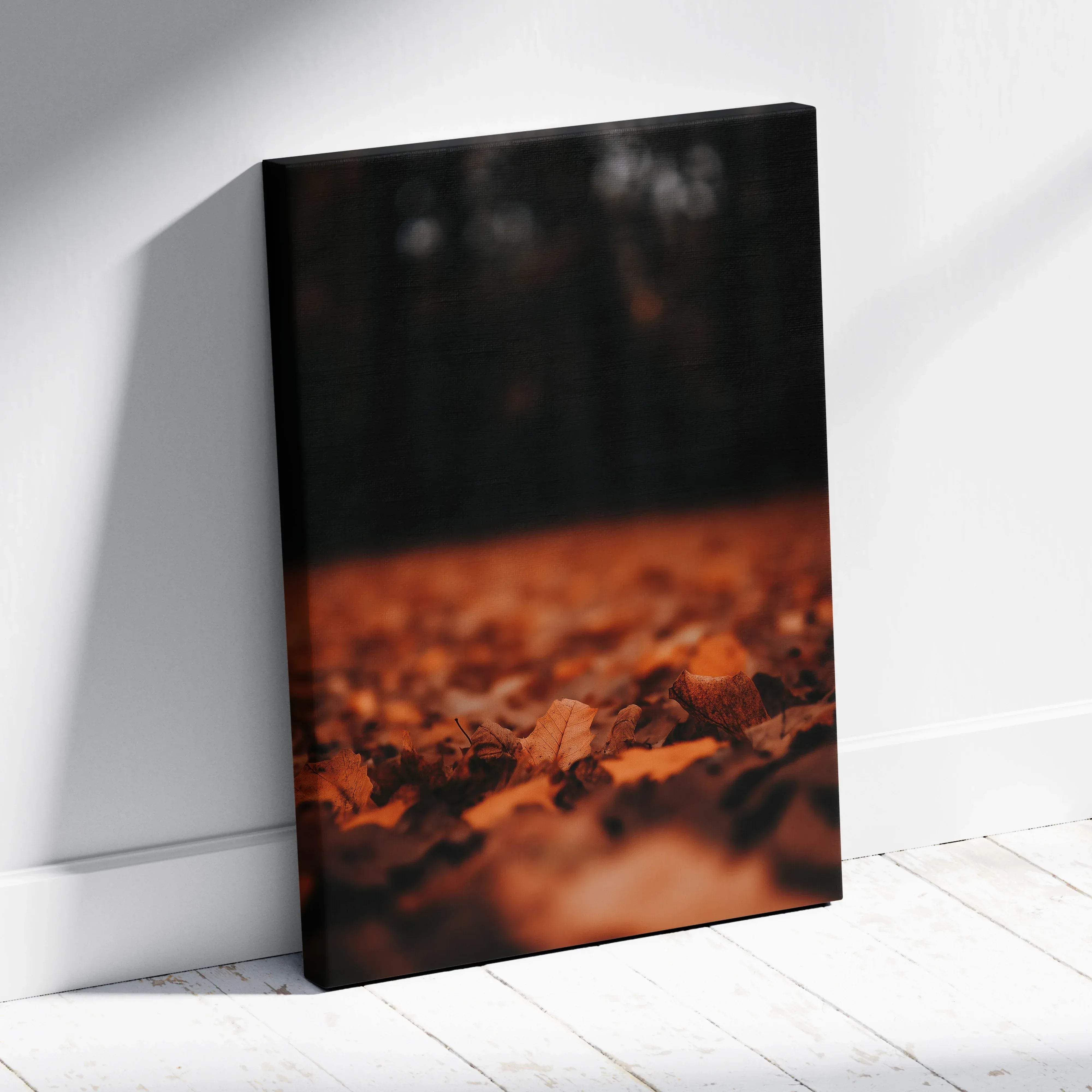 A rectangular canvas print of autumn leaves in warm sepia tones leaning against a white wall