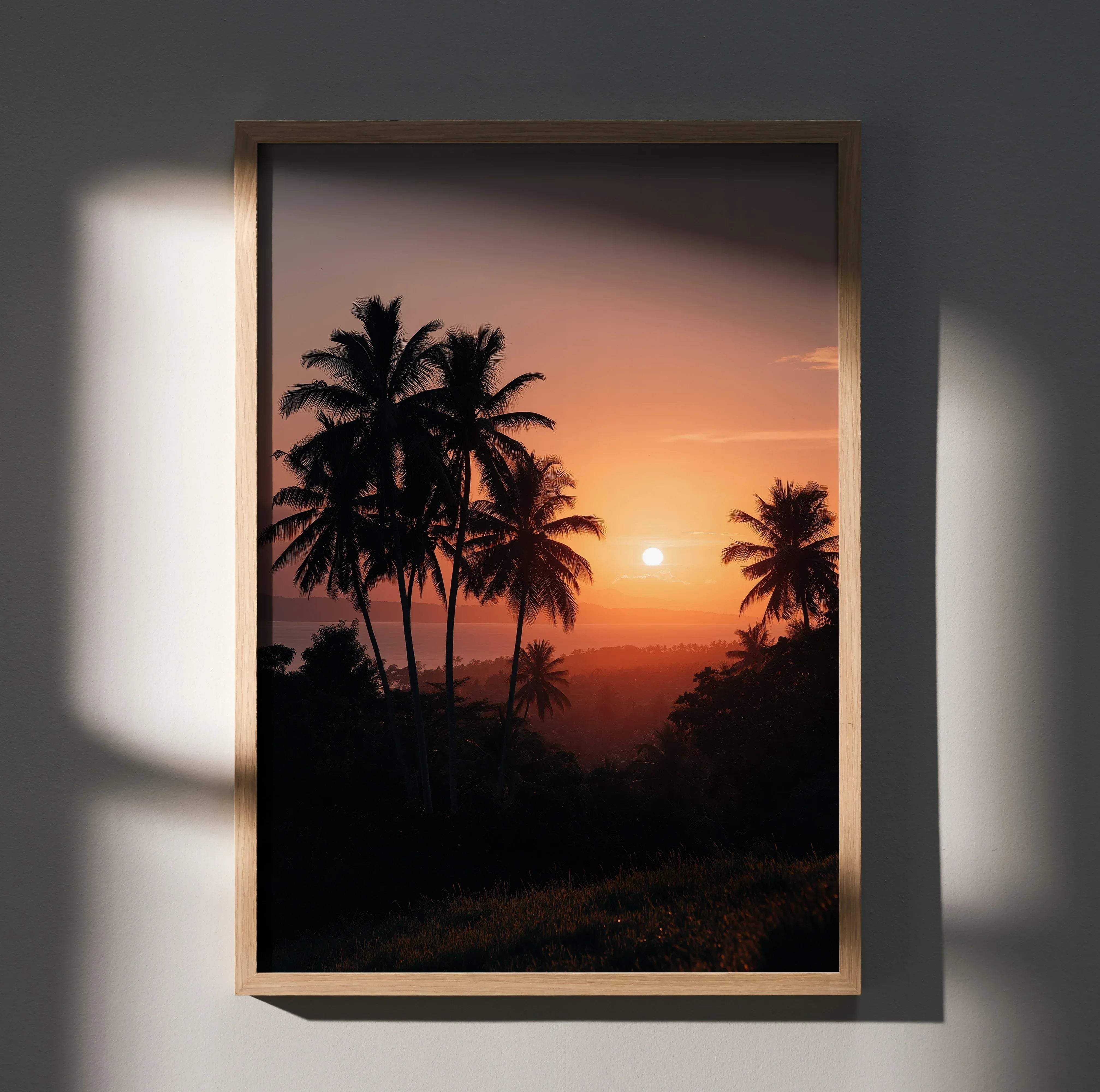 A rectangular wooden-framed art print of a tropical beach sunset with silhouetted palm trees in orange and pink hues