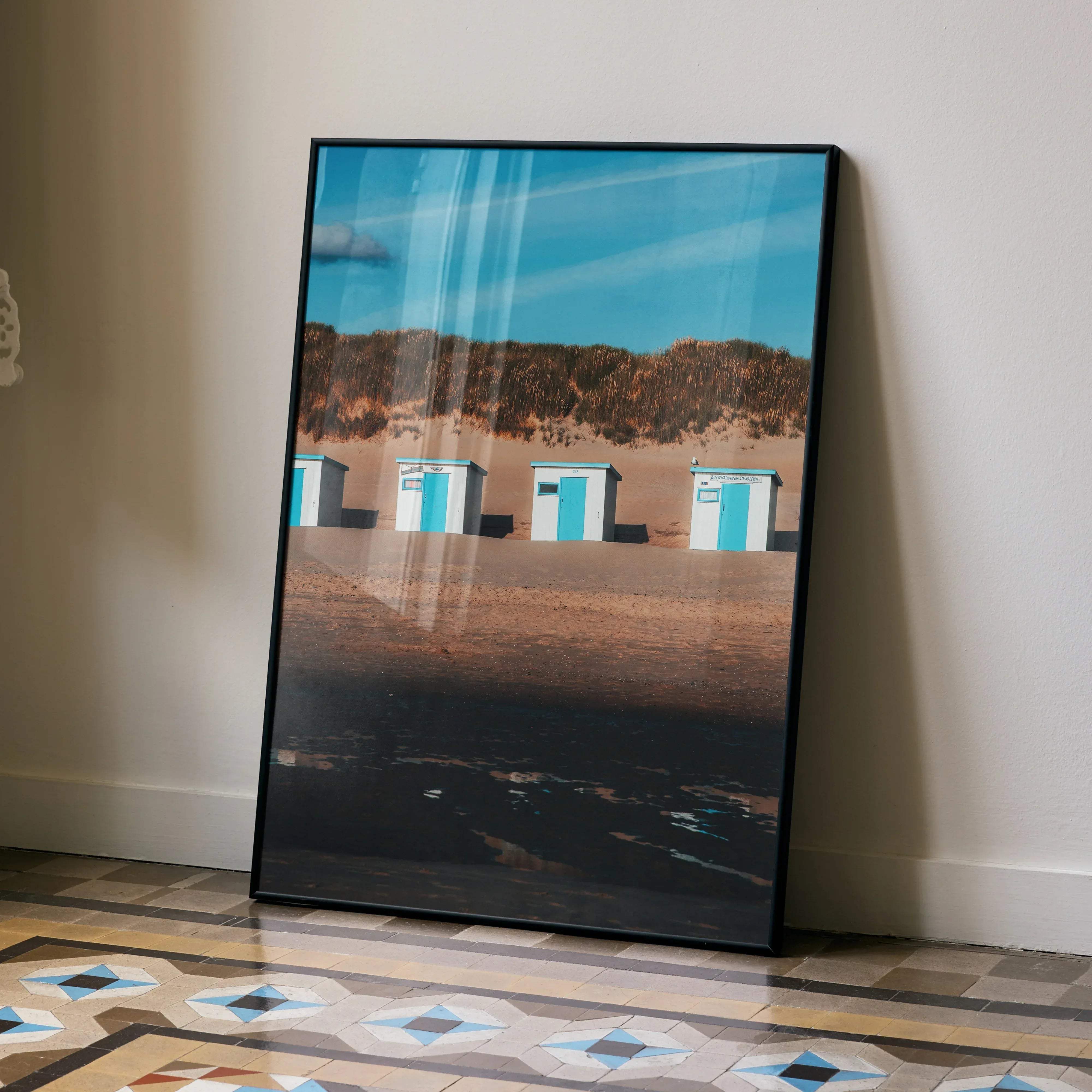 A framed vertical wall art poster featuring turquoise and white beach huts with dunes under a clear blue sky