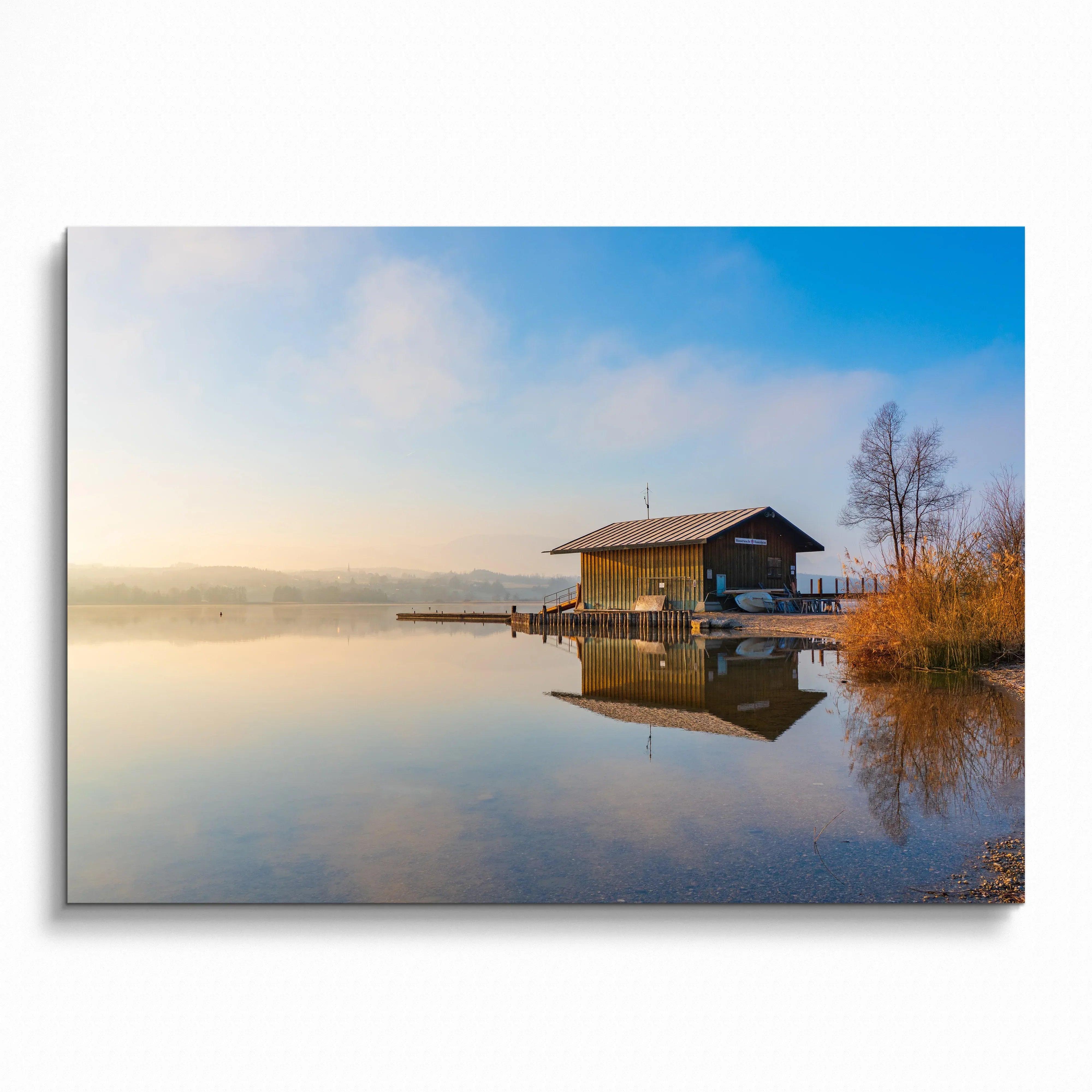 Calm lakeside cabin reflected in still water under soft blue sky wall art poster.