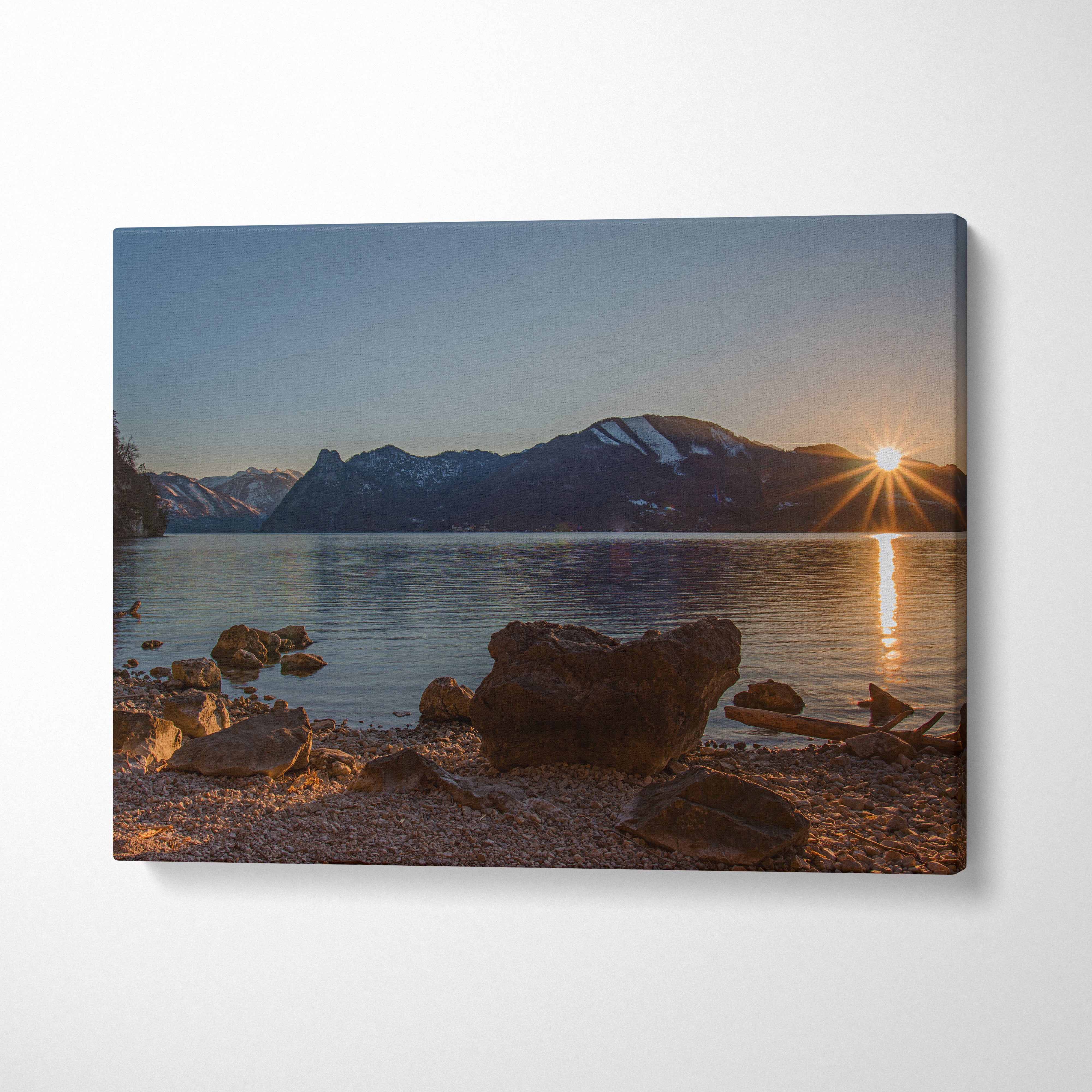 Canvas wall art featuring a mountain sunset with calm lake and sunburst over dark rocky shore.