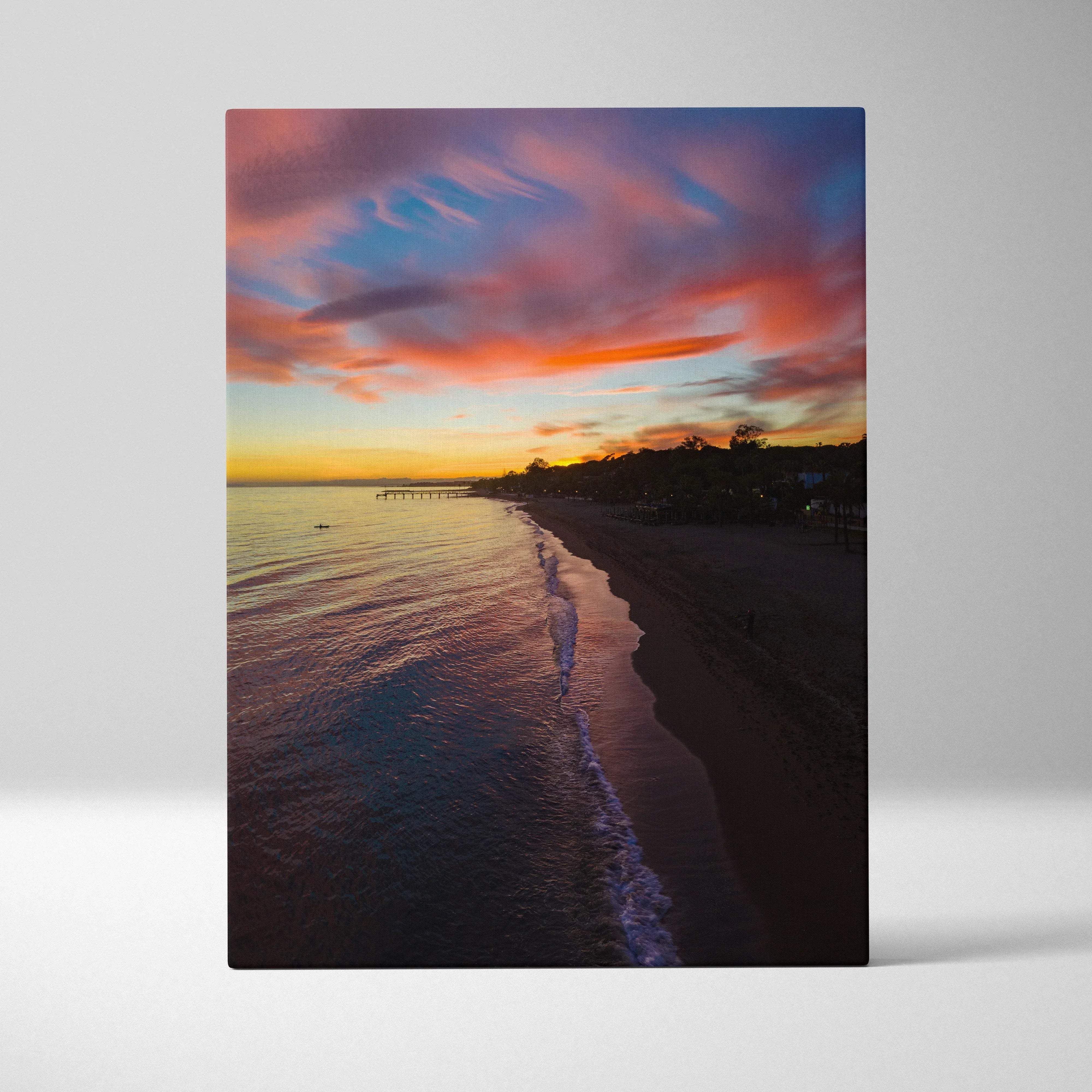 A rectangular canvas print of a vibrant beach sunset seascape with warm orange pink and purple clouds reflecting on water