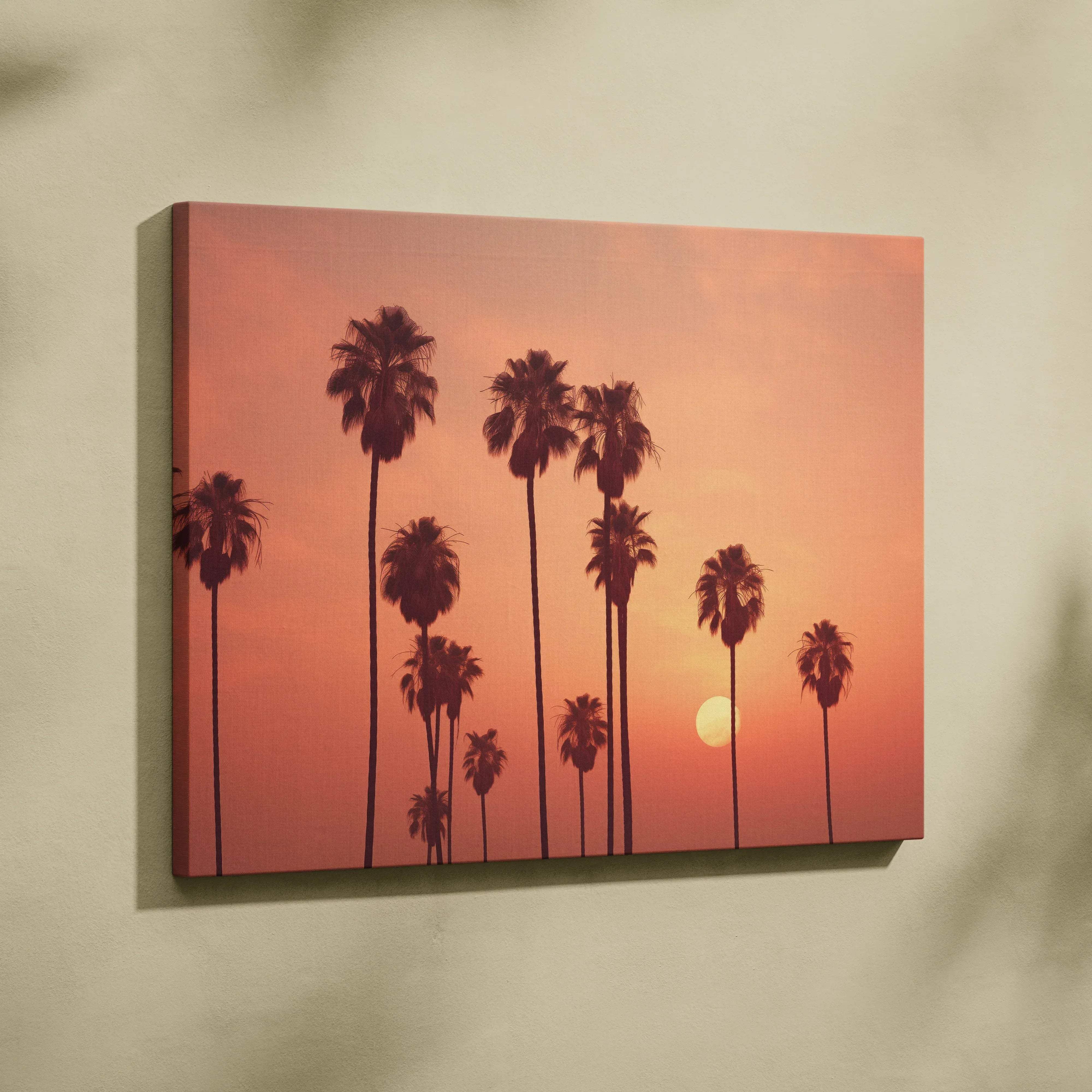 A rectangular canvas wall art featuring silhouetted palm trees against a warm orange and pink sunset sky