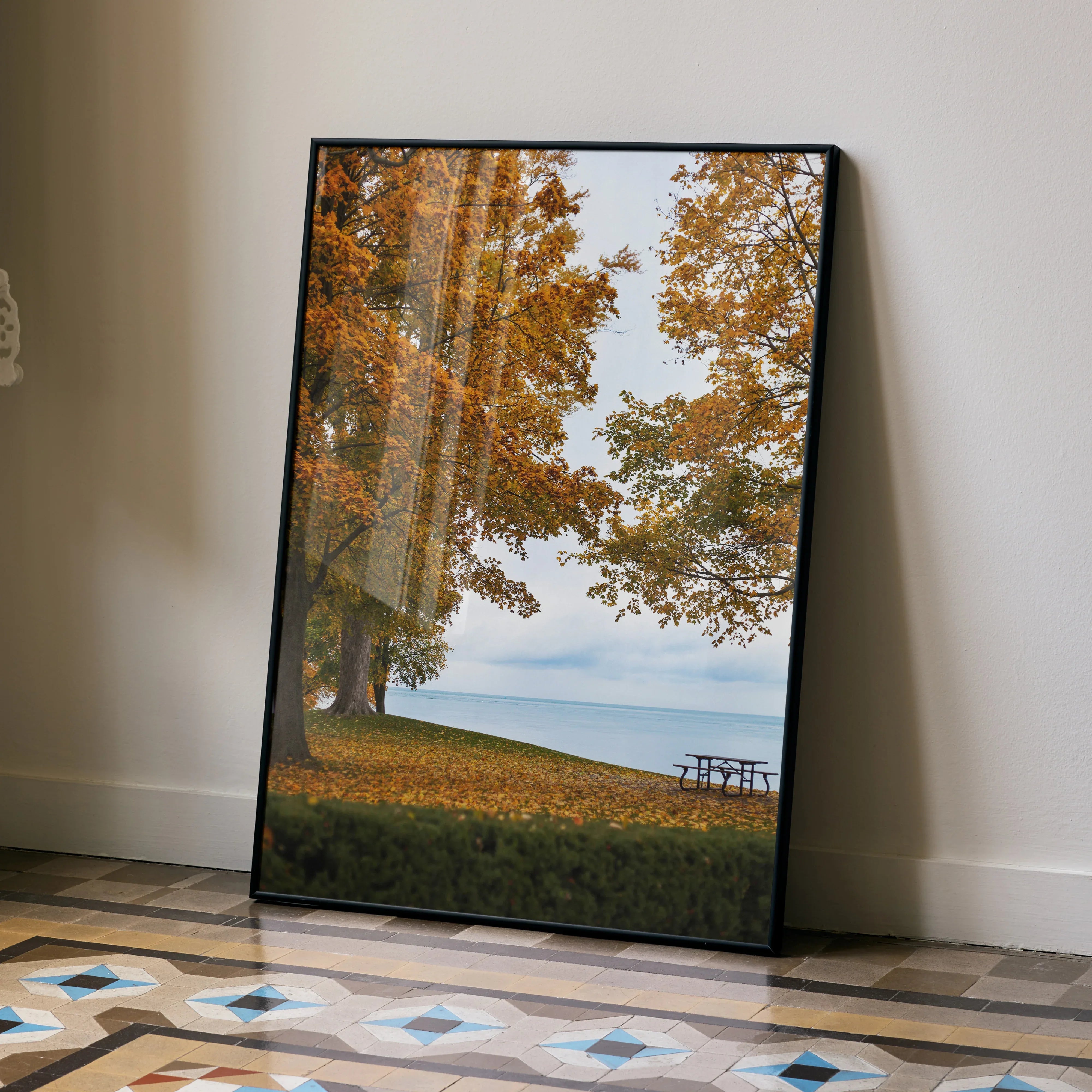 Vertical poster wall art of autumn trees with golden leaves by a lakeside and bench.