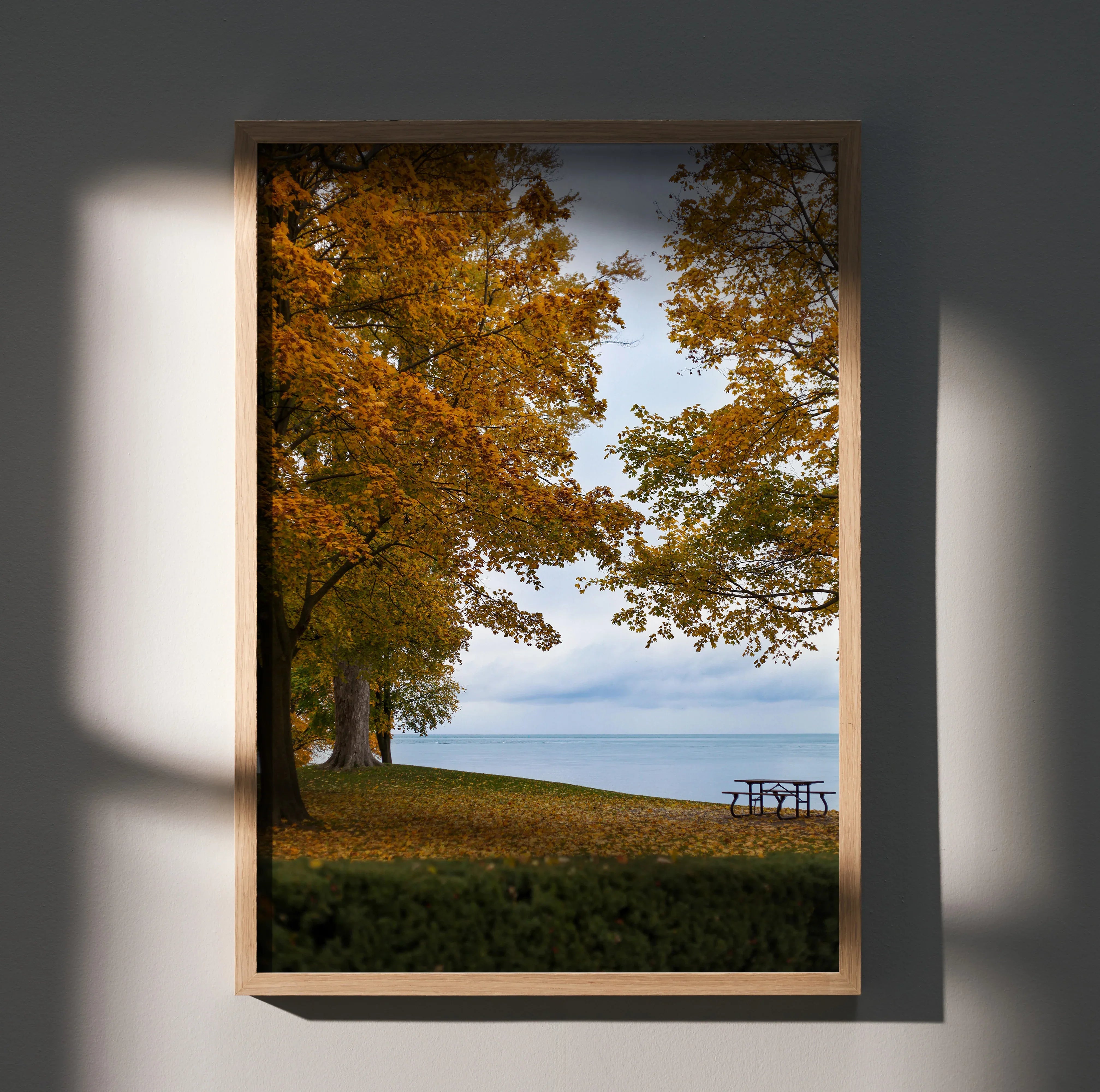 Vertical autumn nature wall art poster featuring golden leaves and a lakeside picnic table under a cloudy sky.