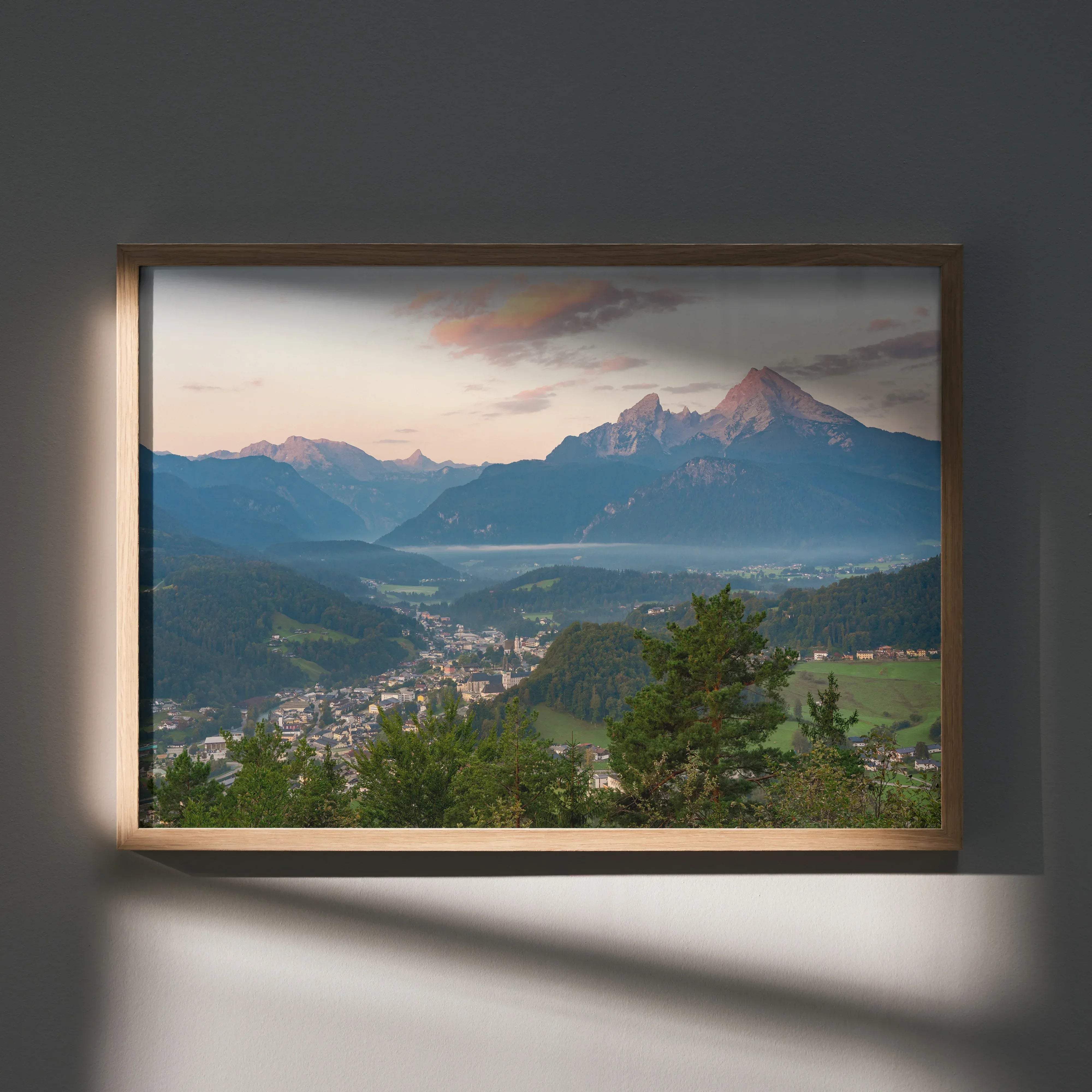A rectangular wooden-framed stunning mountain sunset wall art print with pink and orange hues and green valleys below