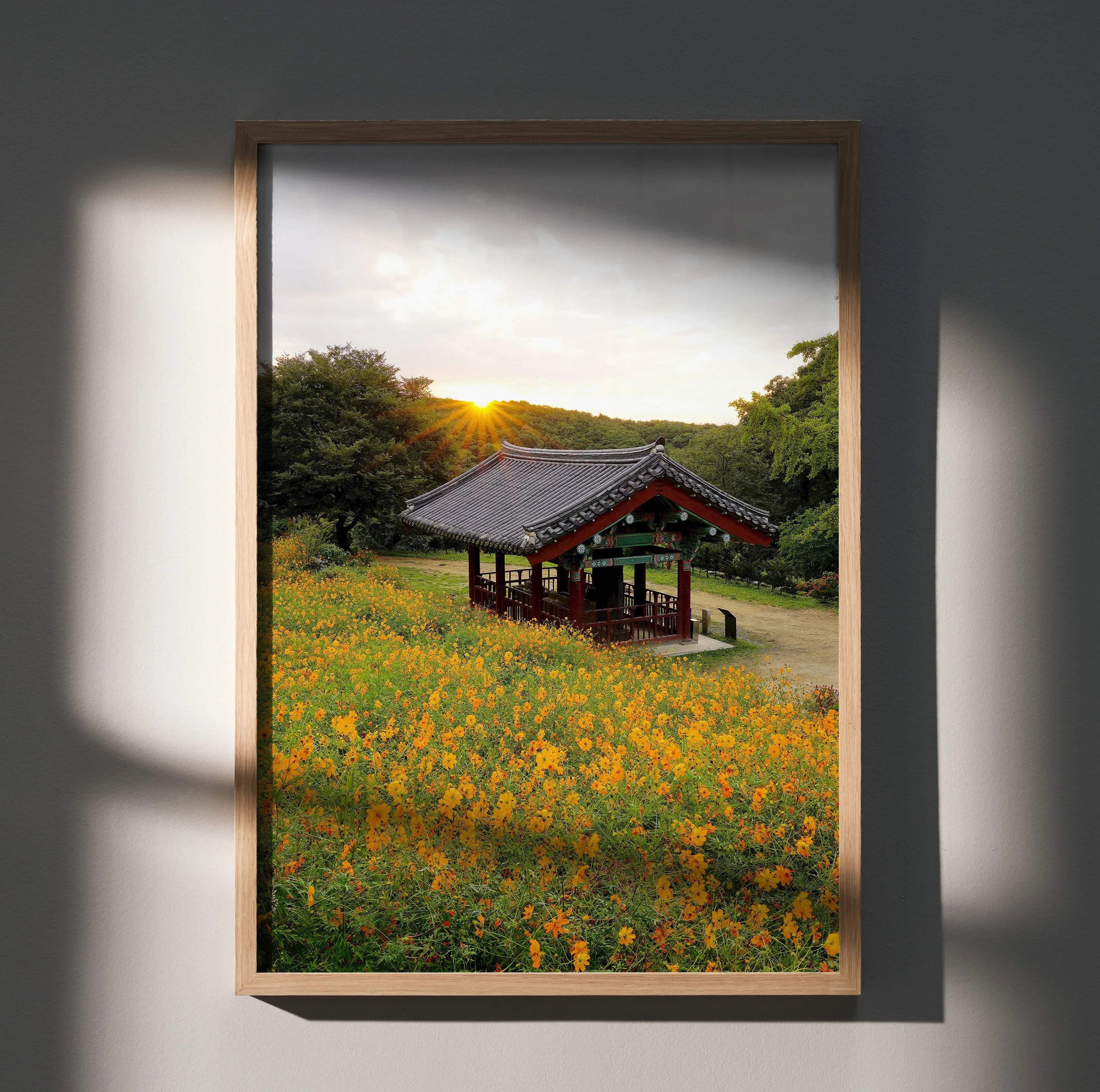 A framed serene sunset urban floral wall art poster featuring a traditional korean pavilion and yellow flowers in a light wood frame