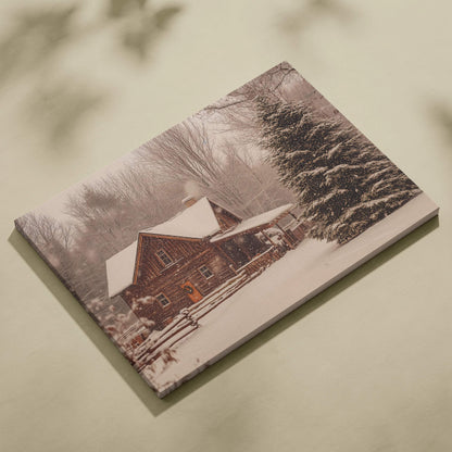 Cozy snowy log cabin with warm amber light in winter forest canvas print